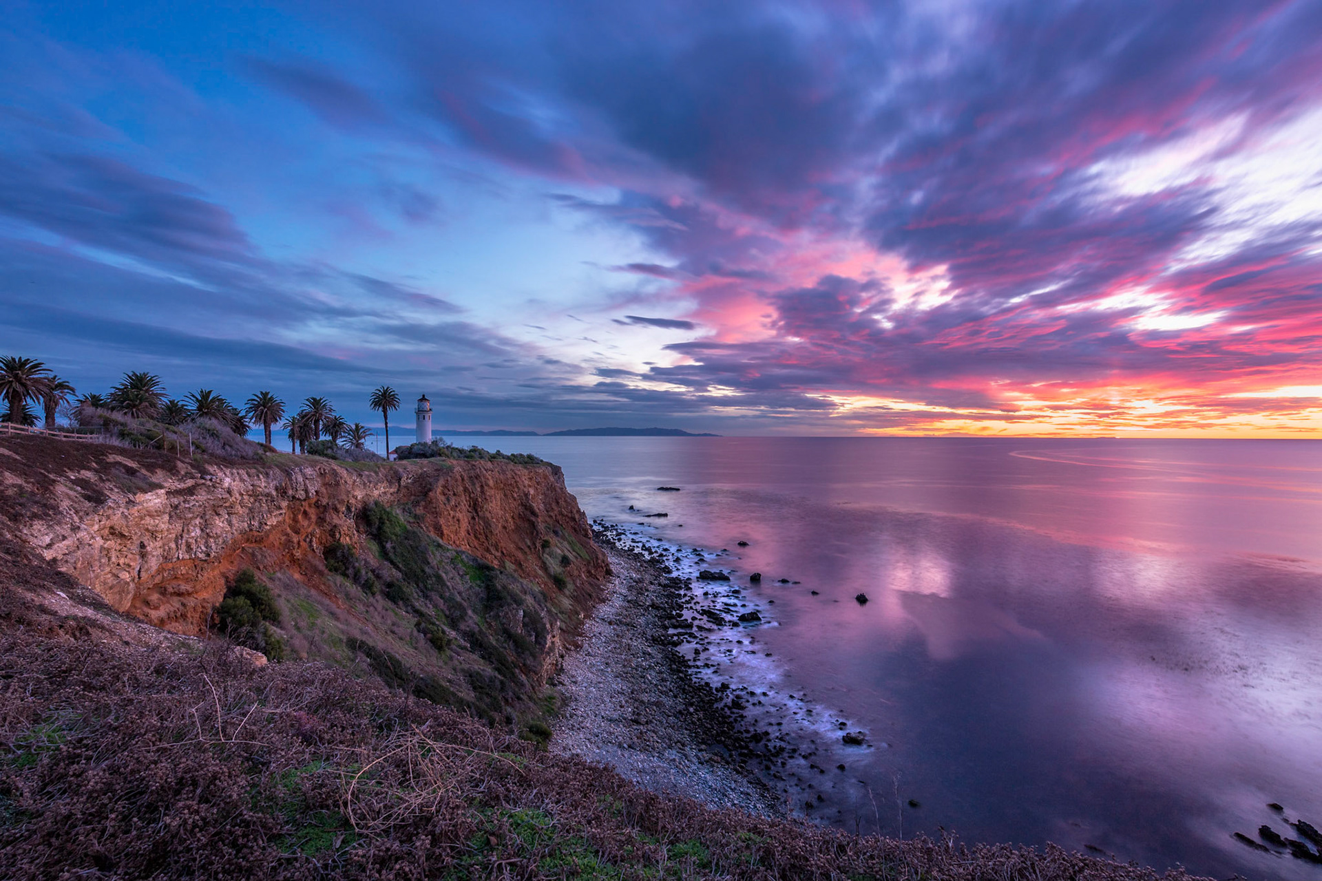 Gorgeous long exposure clifftop view of Point Vicente Lighthouse after sunset with colorful clouds in the sky and calm waves washing onto the rocky shoreline, Rancho Palos Verdes, California