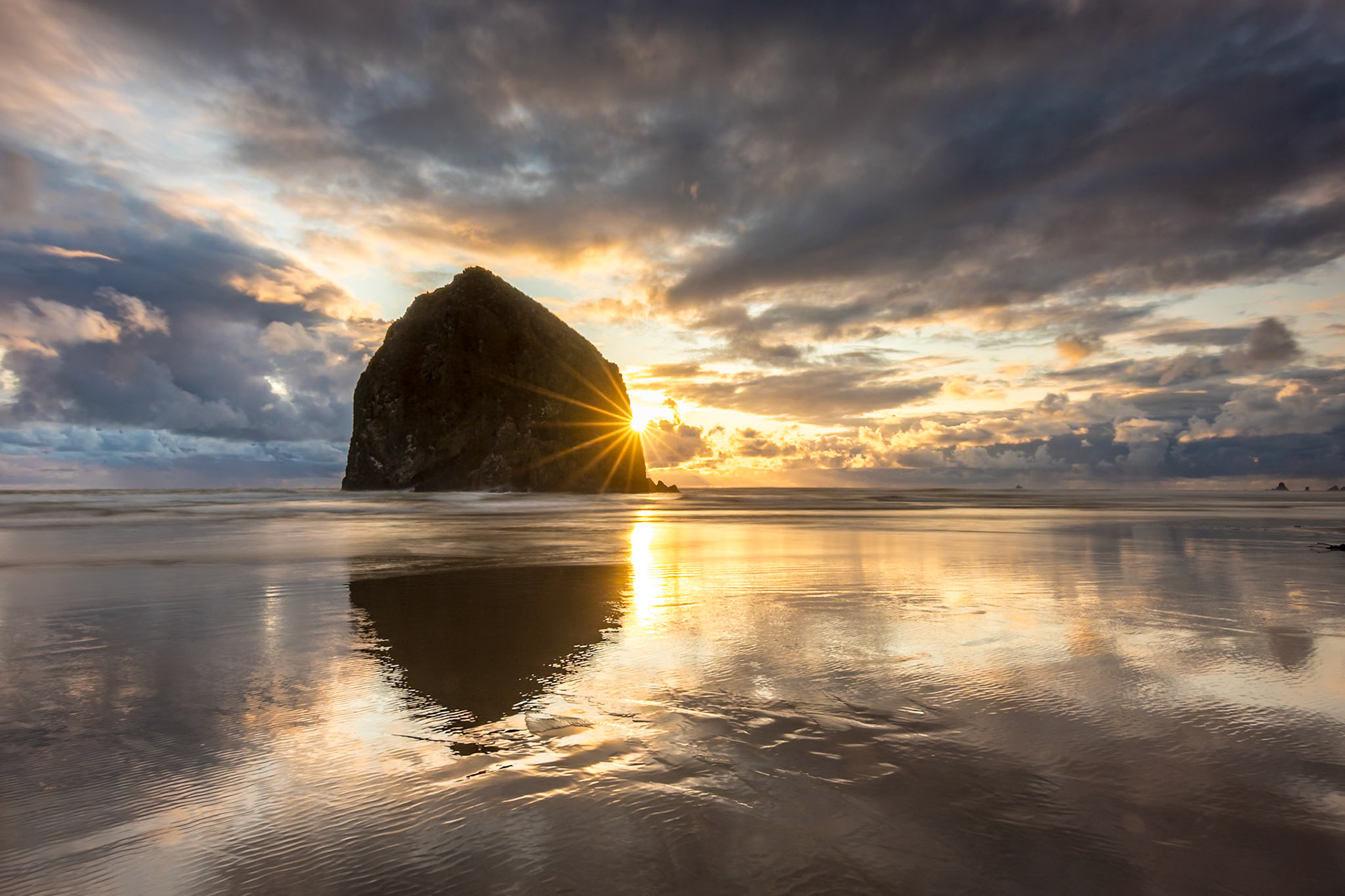 Breathtaking sunset at Haystack Rock on Cannon Beach with colorful sky and reflections from the calm water on the beach