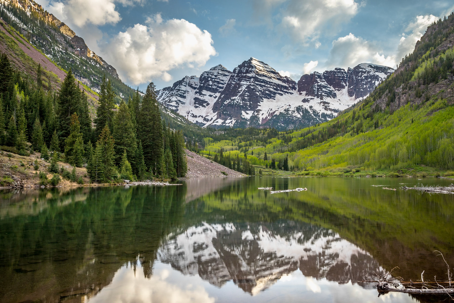 A tranquil lake reflects the majestic mountains and trees in Aspen, Colorado under a partly cloudy sky. Perfect for nature lovers.