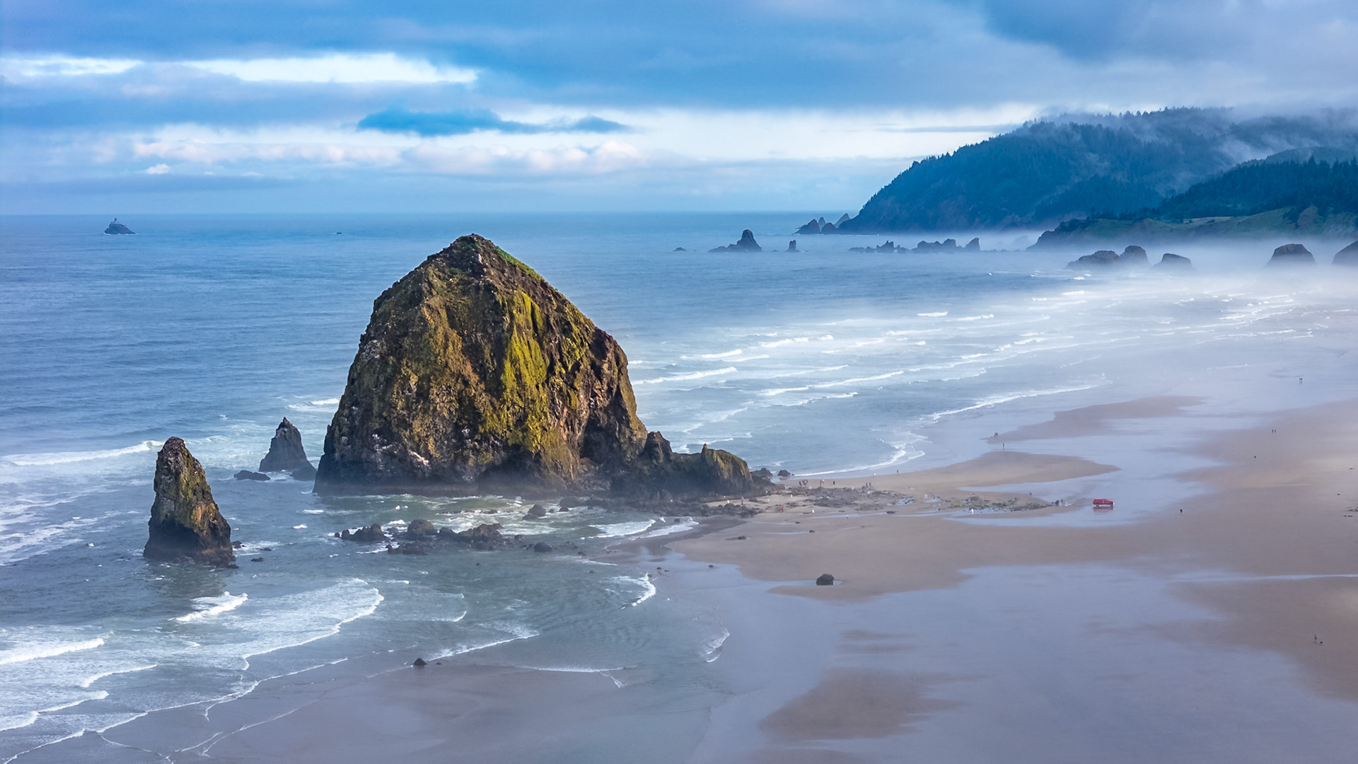 Aerial shot over Cannon Beach, Oregon on a foggy morning, featuring Haystack Rock and moody coastal scenery
