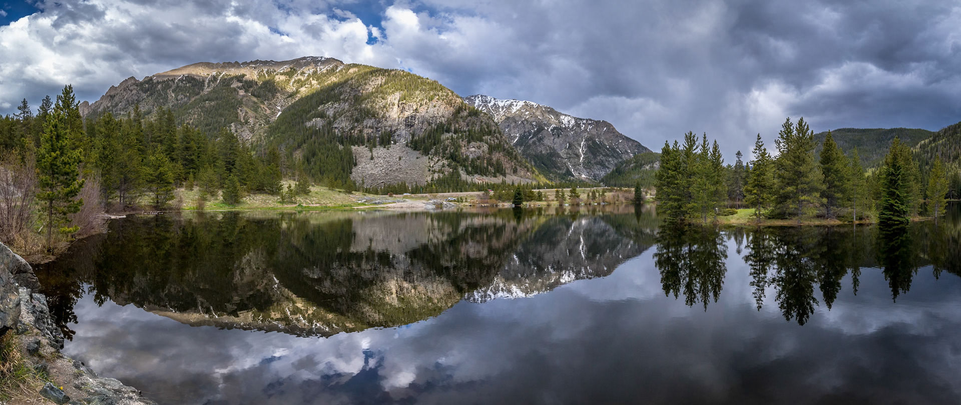 Clear waters of Officers Gulch Pond mirror the stunning Rocky Mountains under a cloudy sky, showcasing serene summer nature in Frisco.