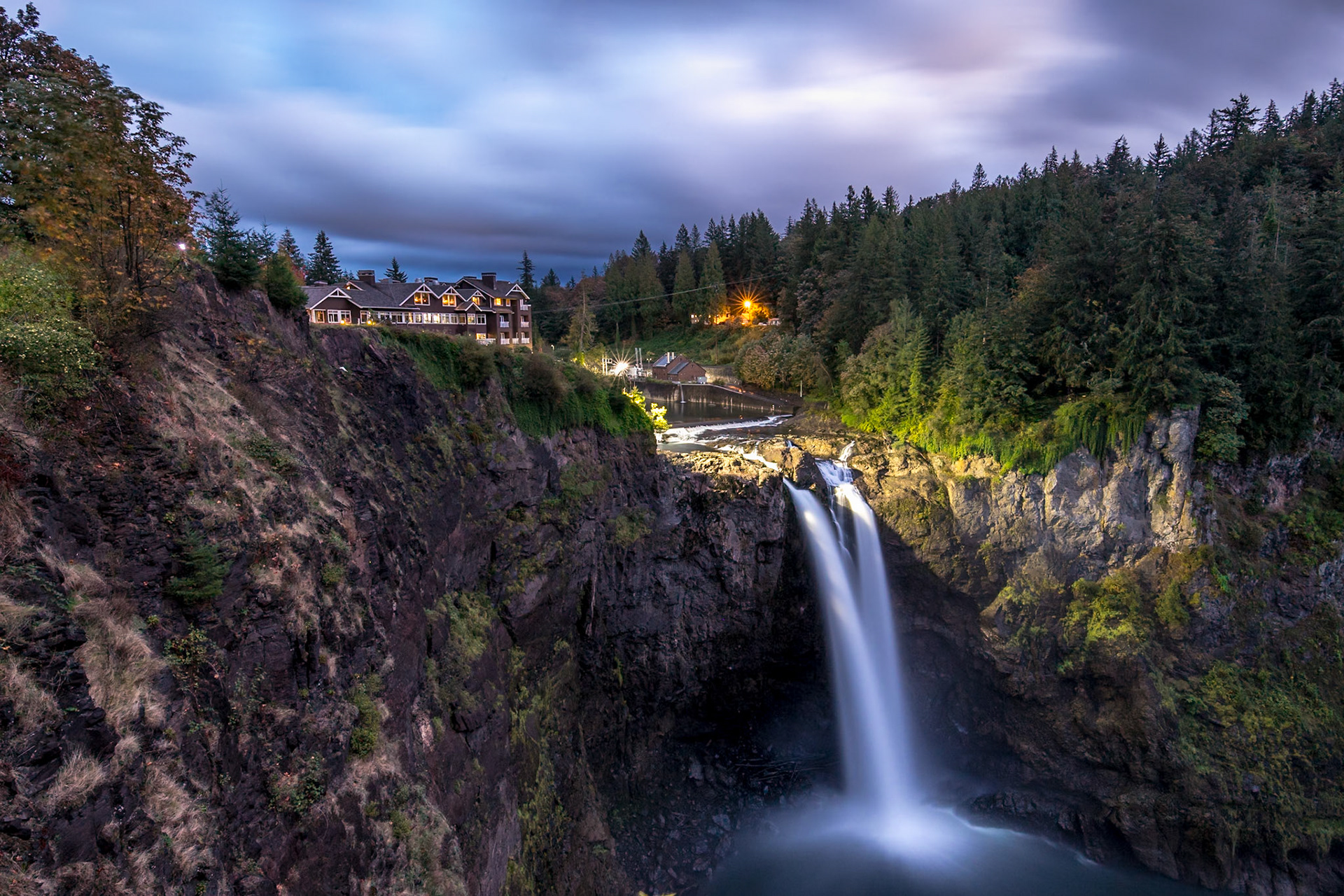 Water pours gracefully over rocky cliffs at Snoqualmie Falls, surrounded by vibrant greenery and dramatic skies in King County, Washington.
