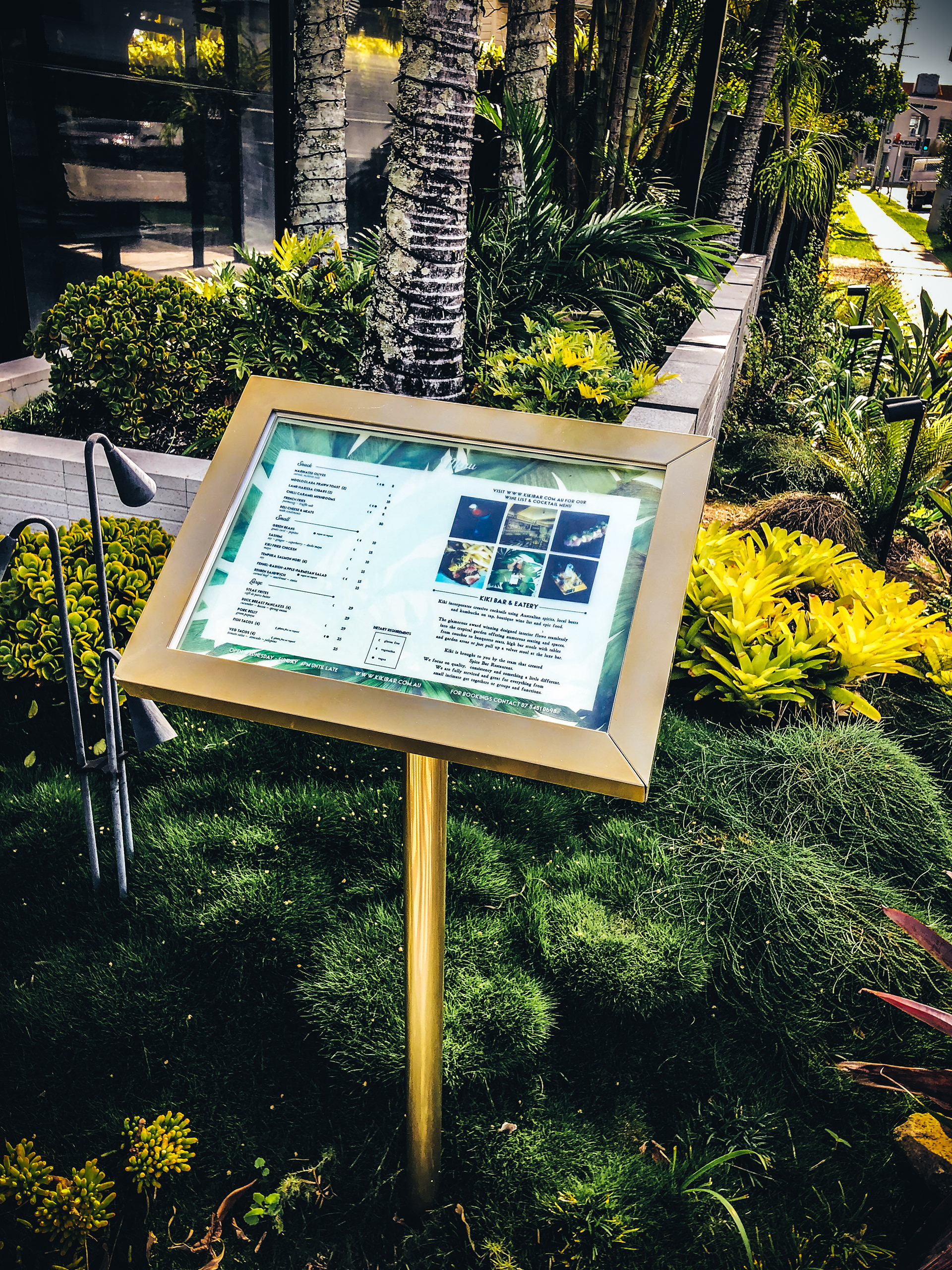 A gold menu board surrounded by a garden