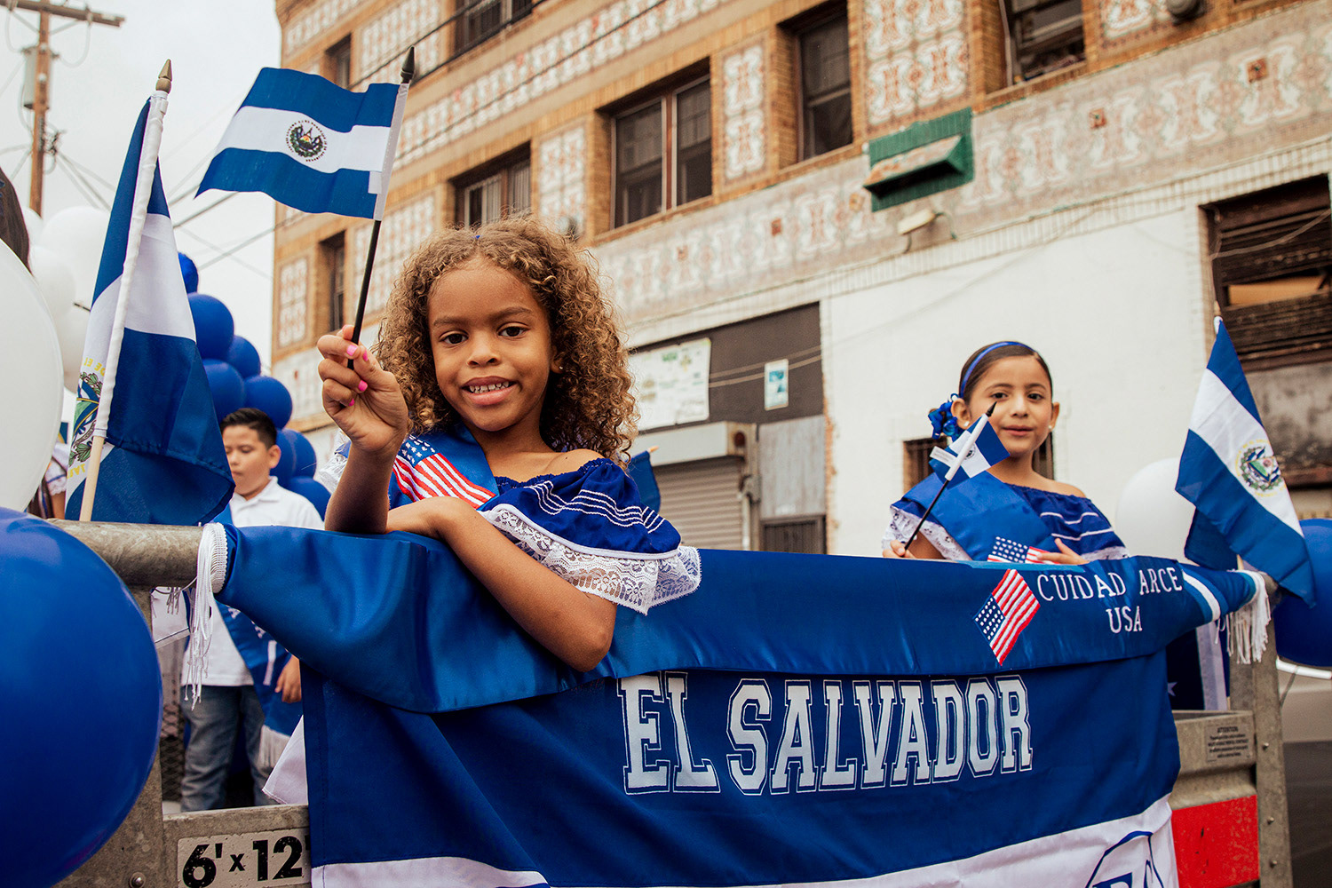 Two young salvadoran girls stand on top of a float waving their flags at the Central American Independence Day Parade in Los Angeles, California on Sunday, September 17th, 2023.
