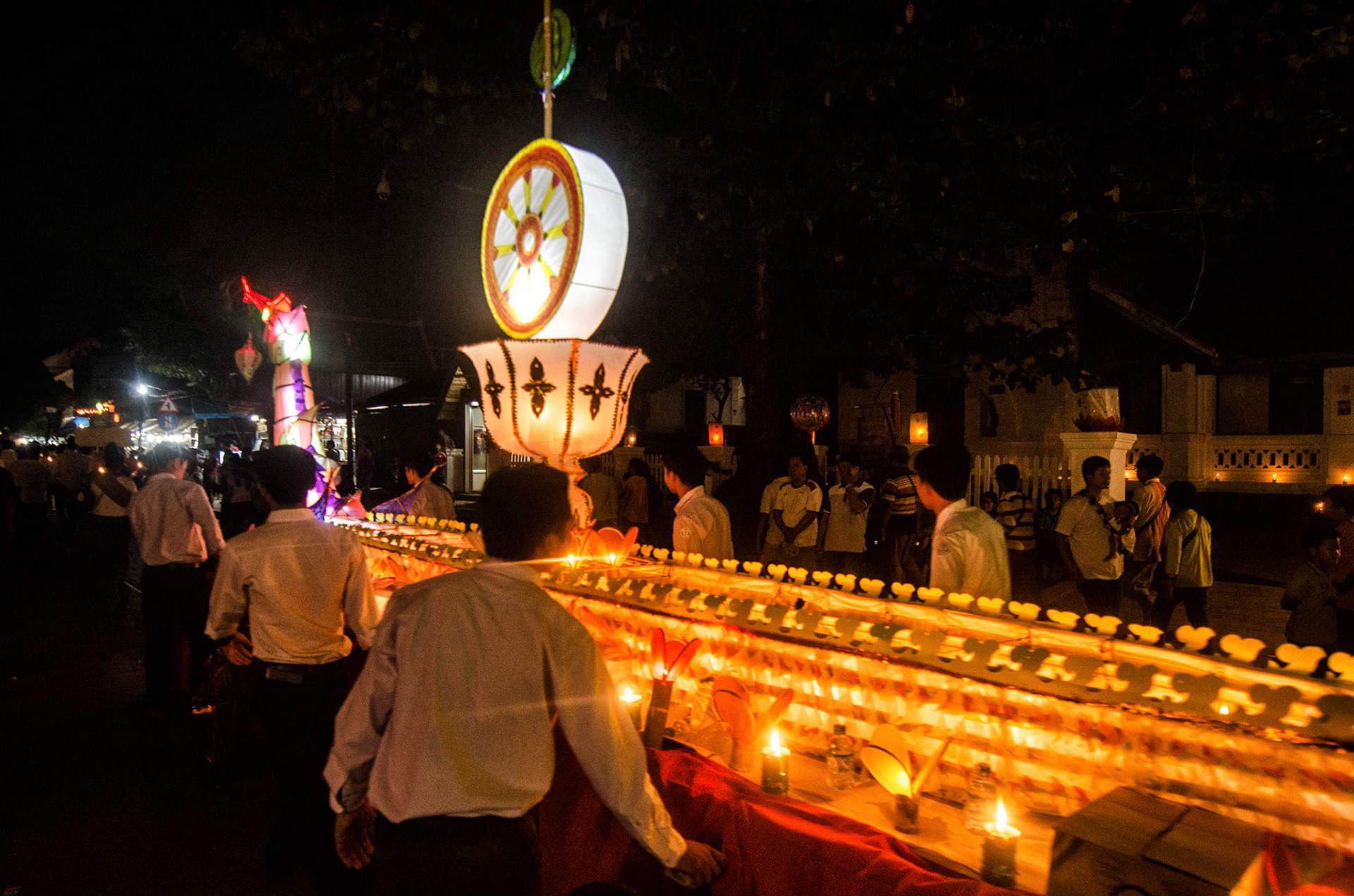 Pessoas carregam barco com velas em procissão. People carry boas with candles on procession. Documentary photographic project about the Fire Boat Festival in Laos. Lanter, culture, tradition, ornament, temple, monk, buddha, buddhism, night, village, story, festa. celebração. Projeto de fotografia documental sobre o Festival do Barco de Fogo no Laos. Lanterna, cultura, tradição, templo, monge, budismo, ornamento, noite, vila, história, party, celebration.