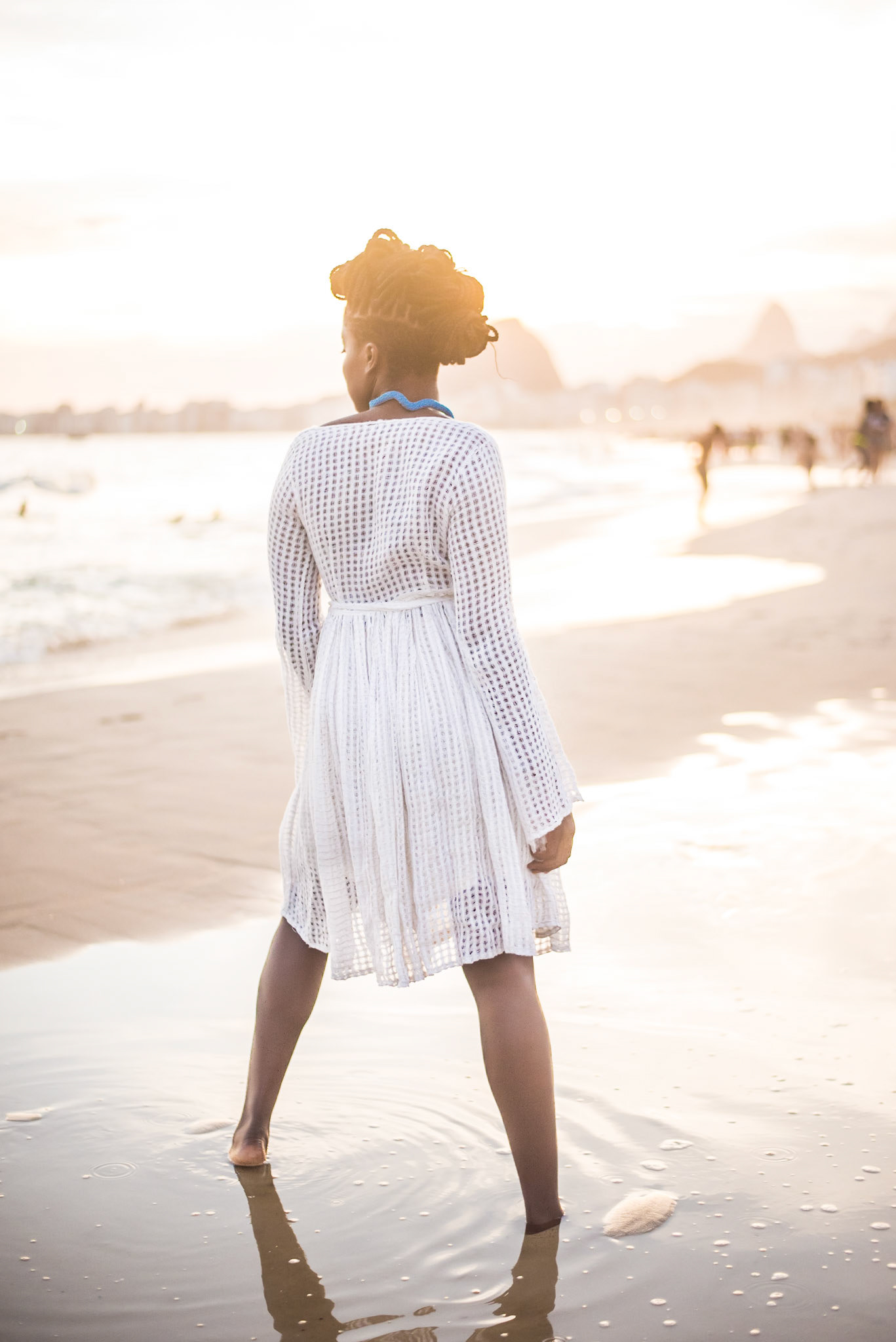 White dress and blue necklace model stands on water and watches the ocean. Modelo de vestido branco e colar azul pisa em agua e observa oceano. woman with large white trousers and golden shell necklace stares at camera. mulher de calça grande e colar concha dourado olha para camera. fashion photography, designer, clothes, dress, accessory, product, still, brand, lookbook, shooting, vibrant, colorful, beach, creative, catalogue, outfit, look.fotografia de moda, design, roupa, vestido, acessório, produto, still, marca, vibrante, colorida, praia, catálogo, rio de janeiro.