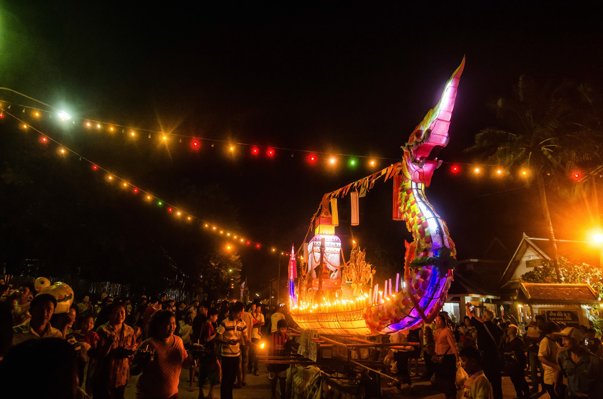 People follow lighted boat on procession. Pessoas seguem barco iluminado em procissão. Documentary photographic project about the Fire Boat Festival in Laos. Lanter, culture, tradition, ornament, temple, monk, buddha, buddhism, night, village, story, festa. celebração. Projeto de fotografia documental sobre o Festival do Barco de Fogo no Laos. Lanterna, cultura, tradição, templo, monge, budismo, ornamento, noite, vila, história, party, celebration.