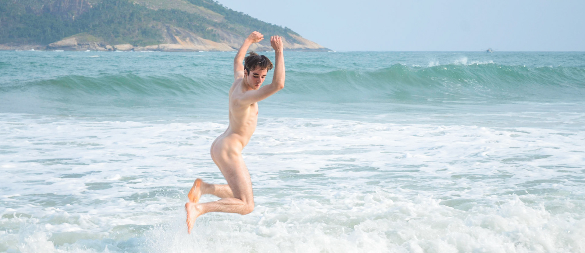 Naked man jumps a wave at beach. Homem nu pula onda em praia. Male nudity, nude, portrait, hairy, beard. Nudez masculina, pelado, barba, peludo, retrato.