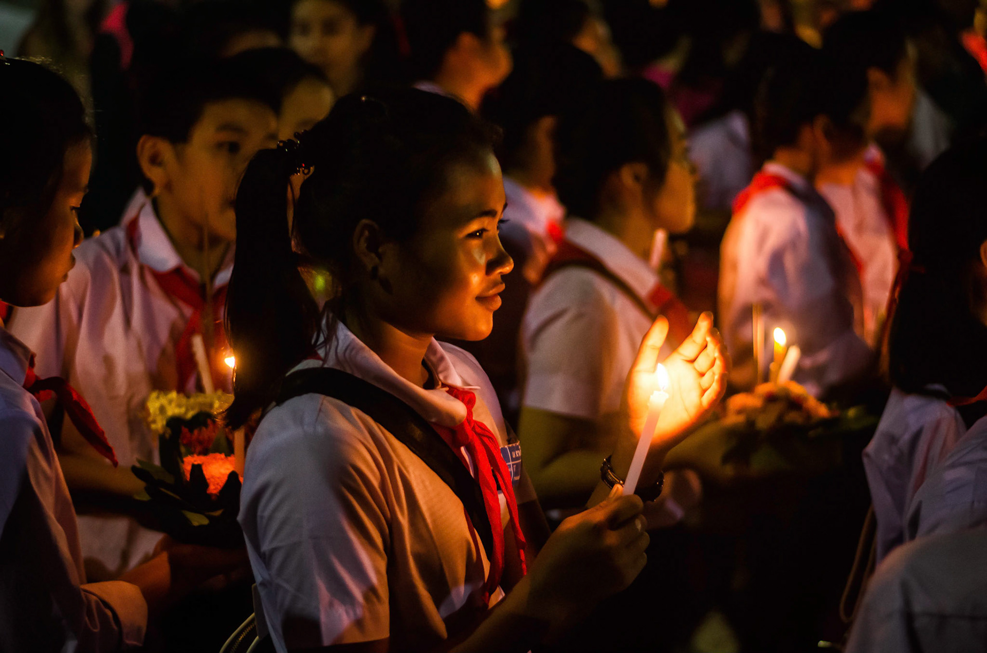 Menina segura vela durante procissão. Girl holds candle during processiopn. Documentary photographic project about the Fire Boat Festival in Laos. Lanter, culture, tradition, ornament, temple, monk, buddha, buddhism, night, village, story, festa. celebração. Projeto de fotografia documental sobre o Festival do Barco de Fogo no Laos. Lanterna, cultura, tradição, templo, monge, budismo, ornamento, noite, vila, história, party, celebration.