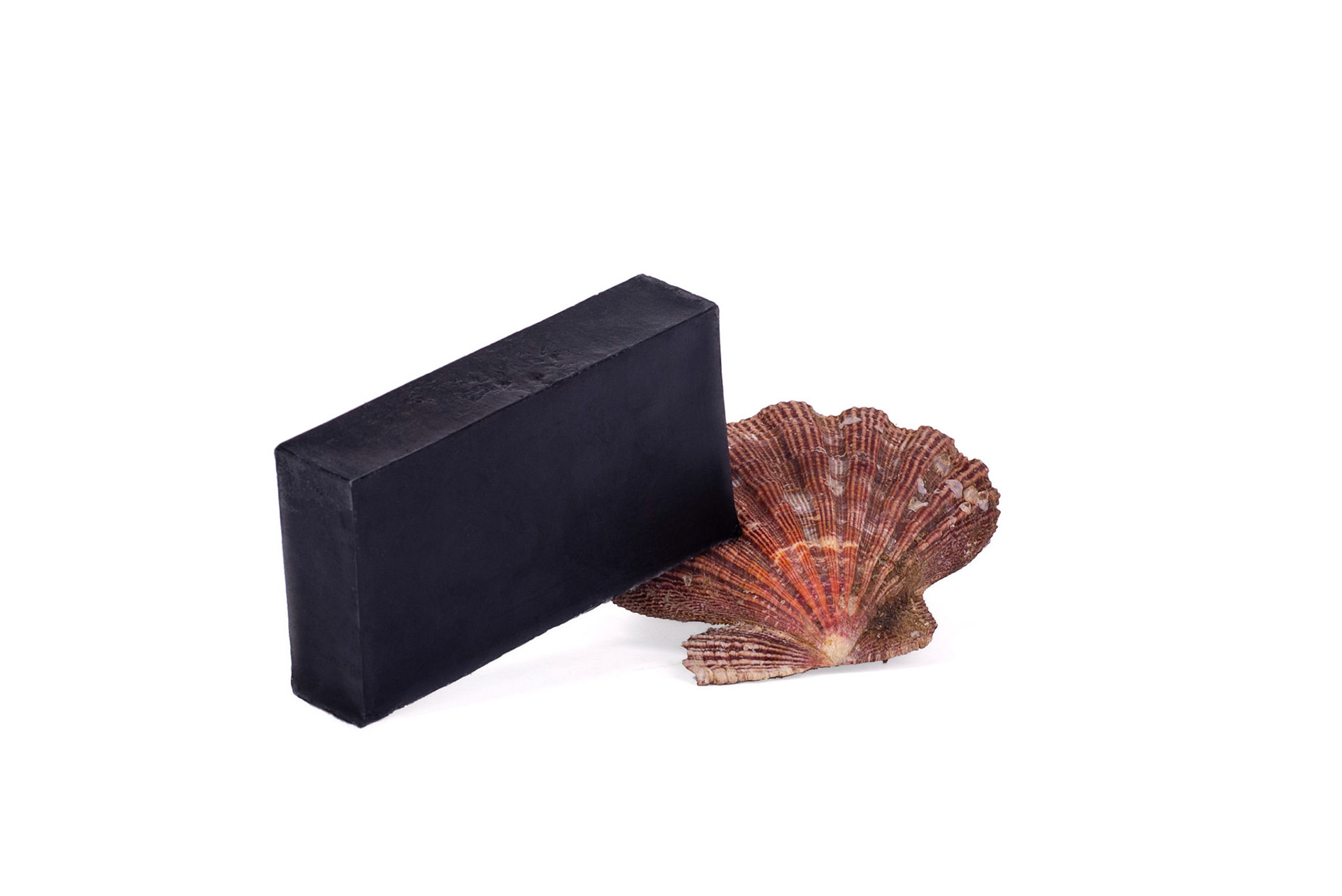 Black coal natural soap with red and orange shell on white studio background. Sabonete carvão junto de concha em fundo branco de estúdio. Still photography, product, ecommerce, e-commerce, shop, online, vibrant, markering, advertising, natural cosmetics, organic. Fotografia produto, loja, vibrante, propaganda, cosméico, orgânico, rio de janeiro. flash, artificial lighting, luz artificial.