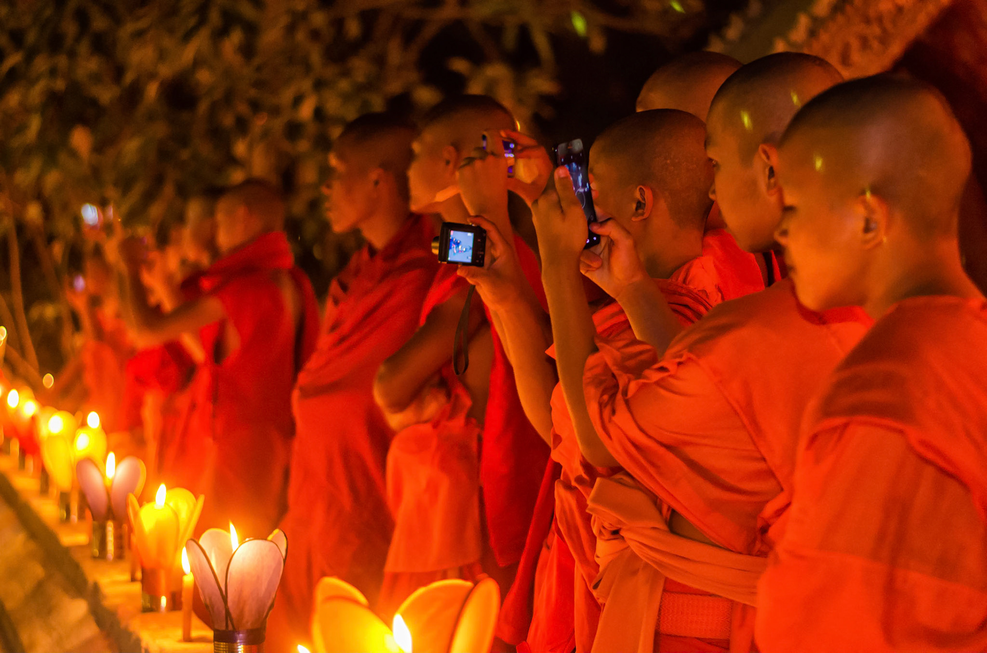 Monks photograph the parade from temple wall. Monges fotografam o festival em muro do templo. Documentary photographic project about the Fire Boat Festival in Laos. Lanter, culture, tradition, ornament, temple, monk, buddha, buddhism, night, village, story, festa. celebração. Projeto de fotografia documental sobre o Festival do Barco de Fogo no Laos. Lanterna, cultura, tradição, templo, monge, budismo, ornamento, noite, vila, história, party, celebration.