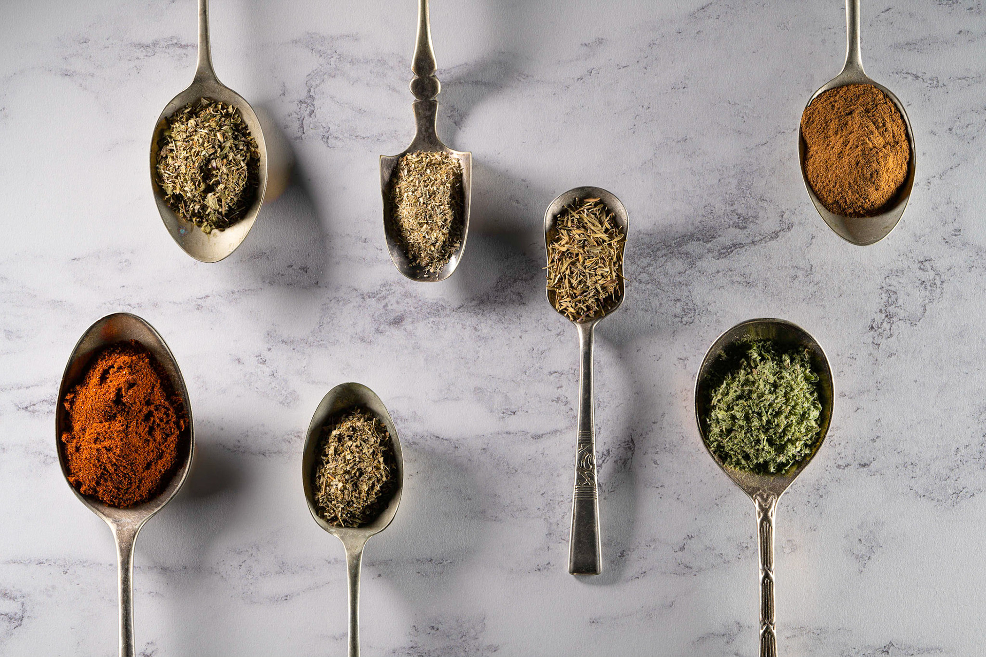 Still-life image of seven spoons with herbs and spices