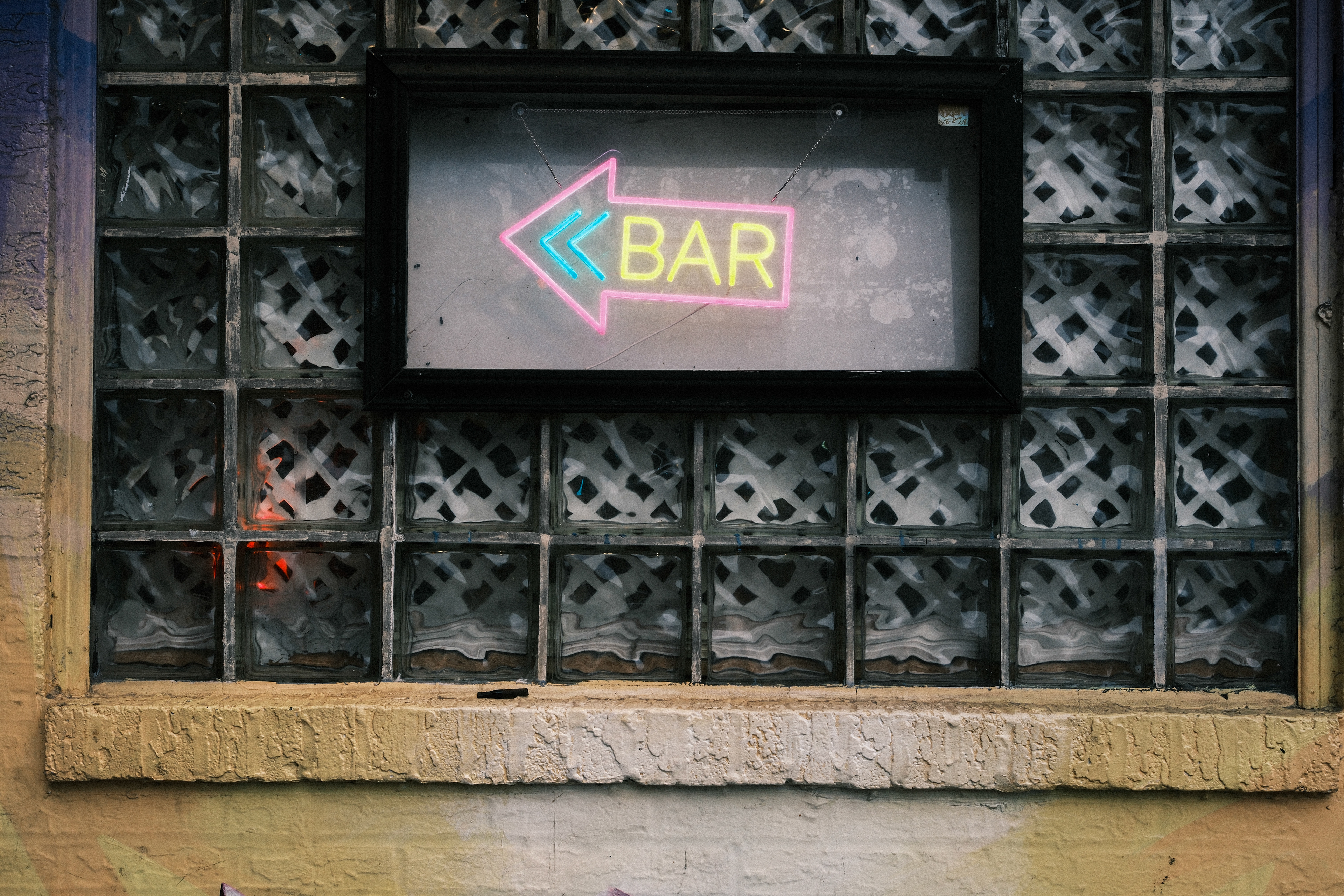 Neon bar sign pointing left beside  glass block windows on a Philadelphia street