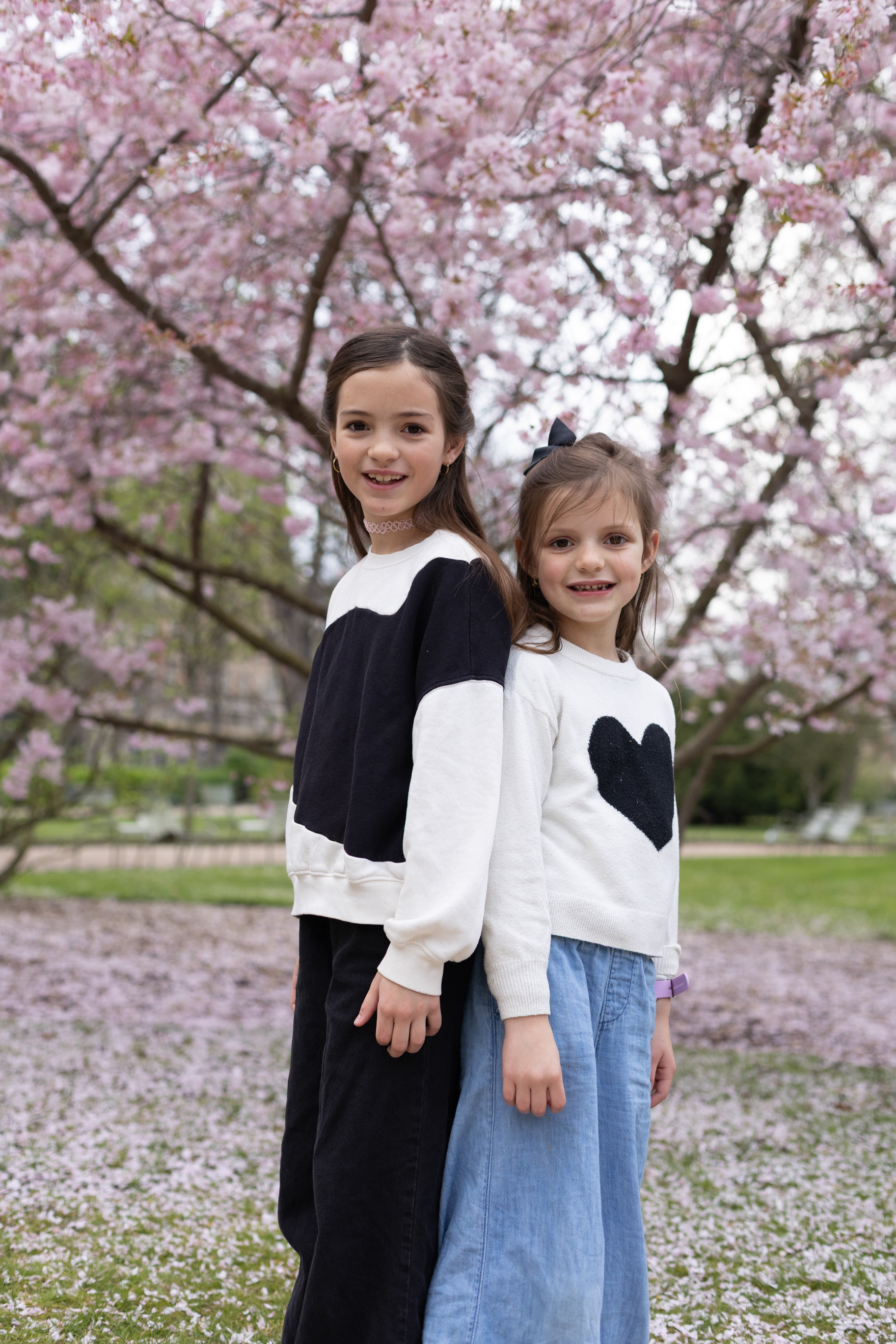 Two young girls posing against blooming pink trees in the Luxembourg Gardens, Paris.