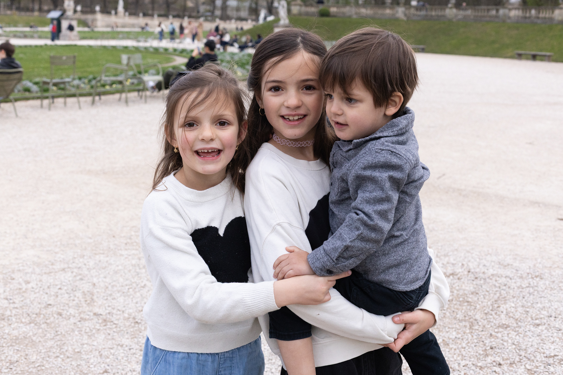 Three children posing together in the blooming Luxembourg Gardens during a professional spring photoshoot in Paris.