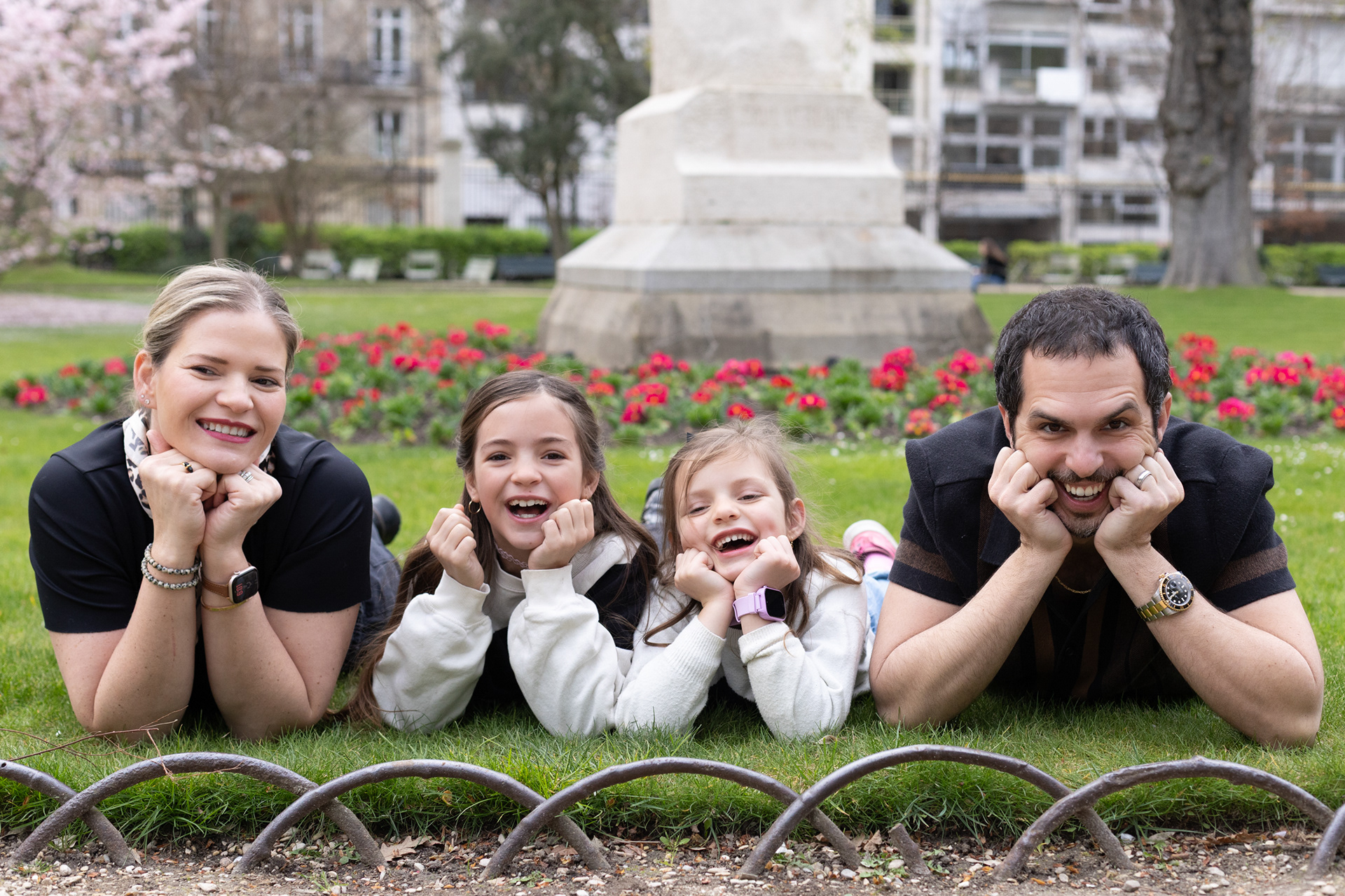 Happy family of four having fun and laughing on the lawn of Luxembourg Garden in springtime, professional Paris photography.