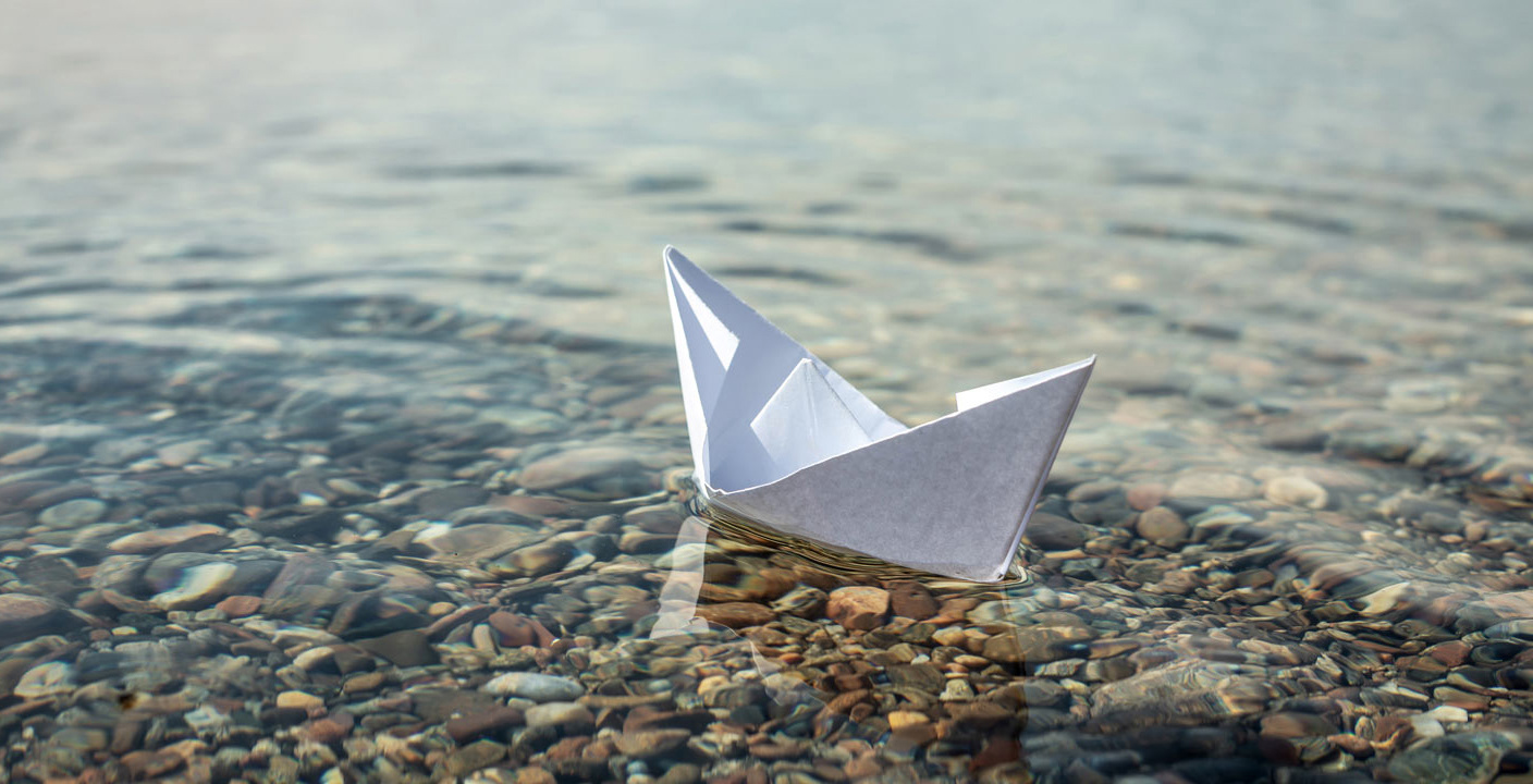 White paper boat in the clear water of large lake with a stony bottom @ Adobe Stock