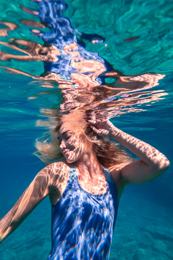 Şahika Ercümen underwater with her head breaking the surface, creating shimmering reflections and light distortions.