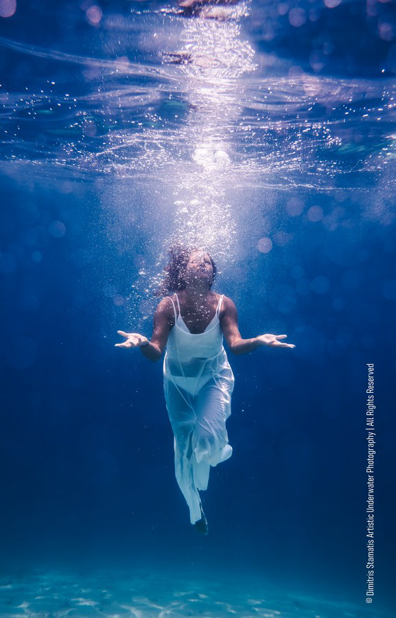 A woman in a white garment floating underwater with bubbles rising toward the surface.
