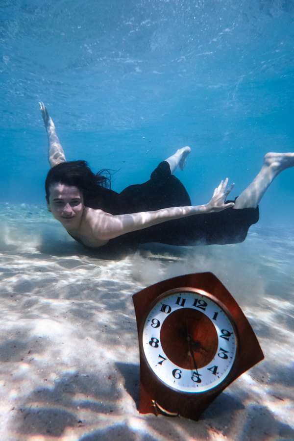 Underwater scene with Eleftheria Bargiota swimming above a clock on the seabed, created for the “Treis Epoxes” album visuals.
