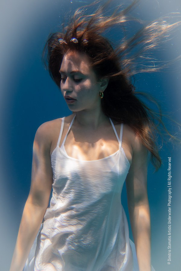 A young girl underwater in a white dress with hair floating around the face.