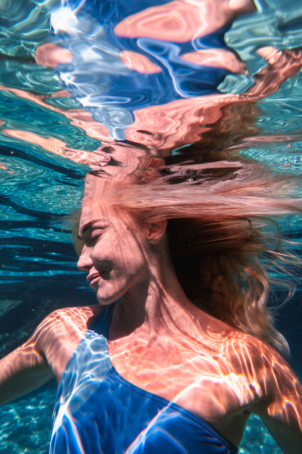 Şahika Ercümen partially submerged underwater with shimmering surface reflections and sunlit patterns.