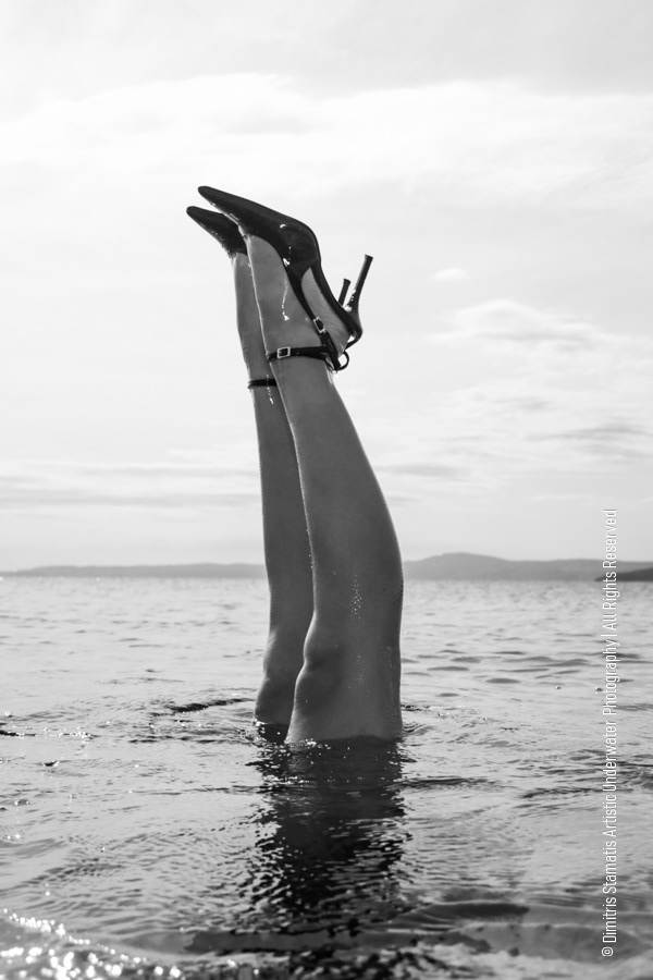 Legs of a girl doing an underwater handstad wearing high heels.