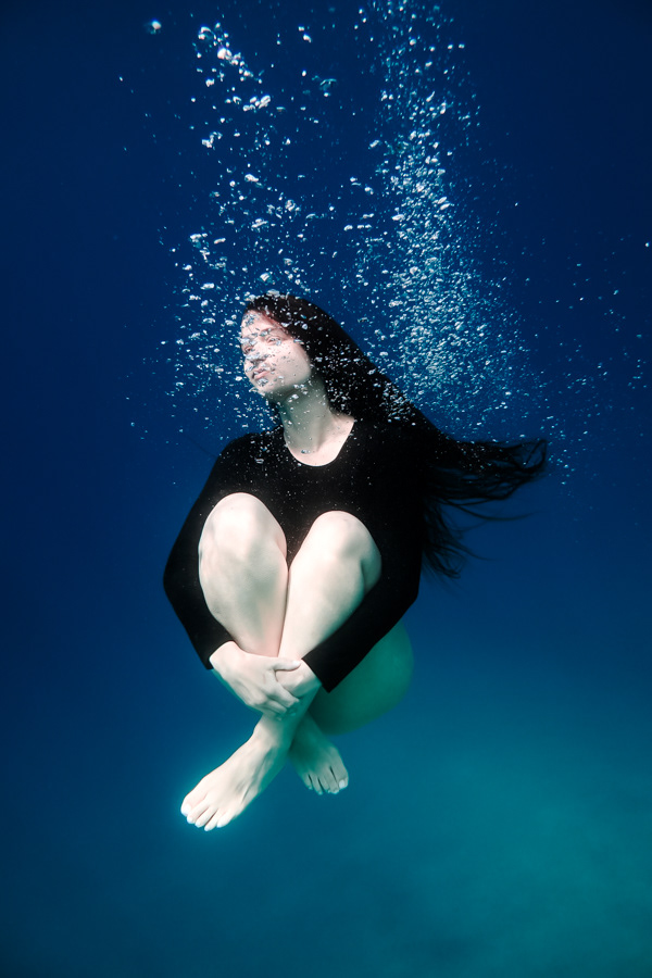 Eleftheria Bargiota floating underwater in a curled pose surrounded by rising bubbles, created for the “Treis Epoxes” album visuals.