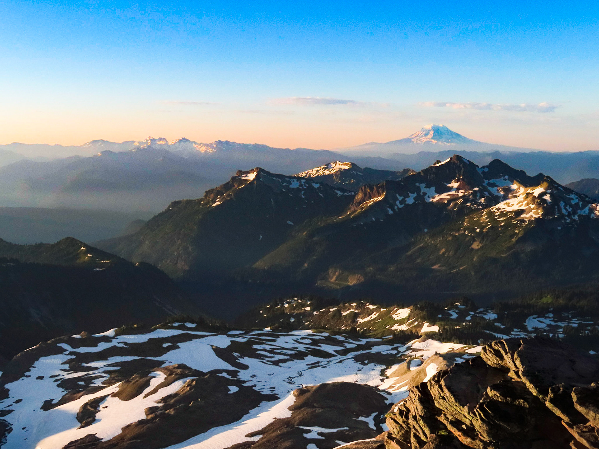 The Tatoosh Range illuminated in the early morning sunrise, with Goat Rocks Wilderness and the Mt Adams volcano looming in the bakcground.