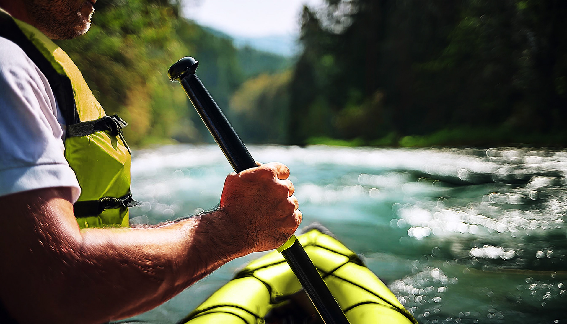 A man holds a paddle handle in front of a raft on a river.
