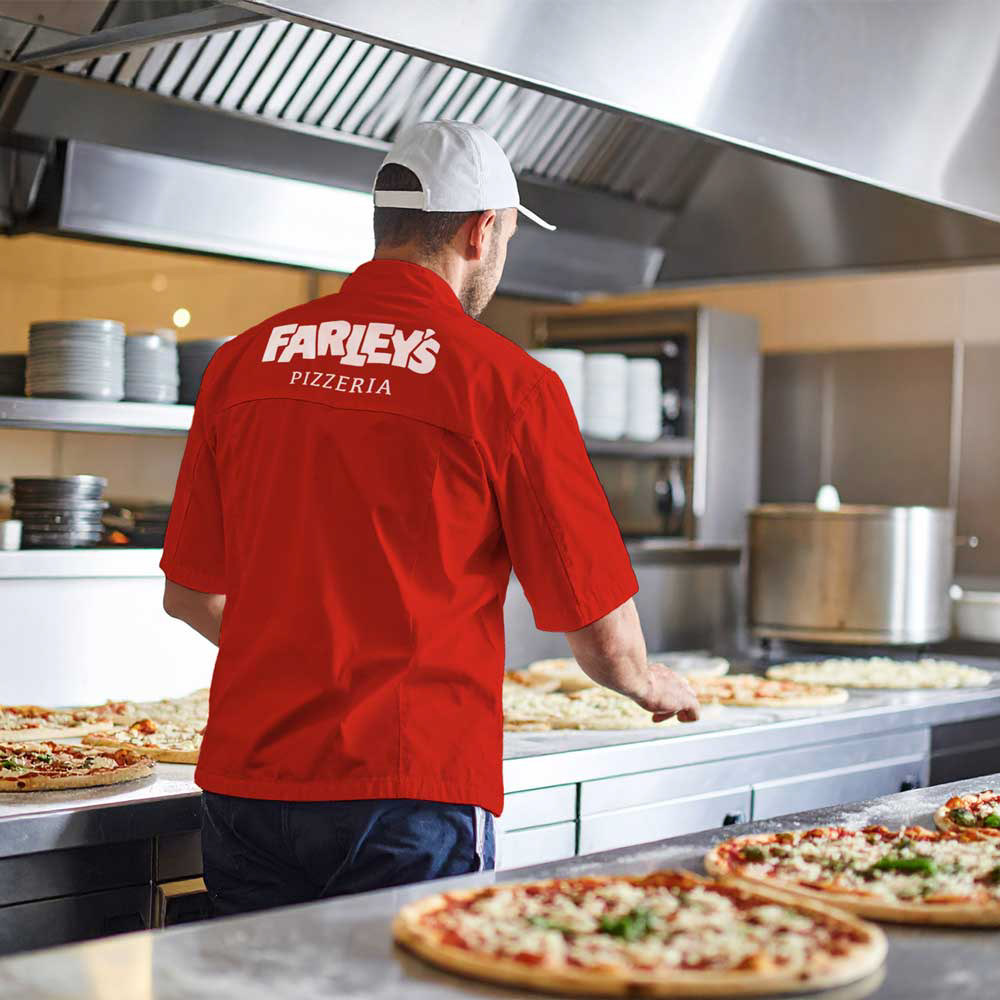 A cook stands in a pizza line kitchen.
