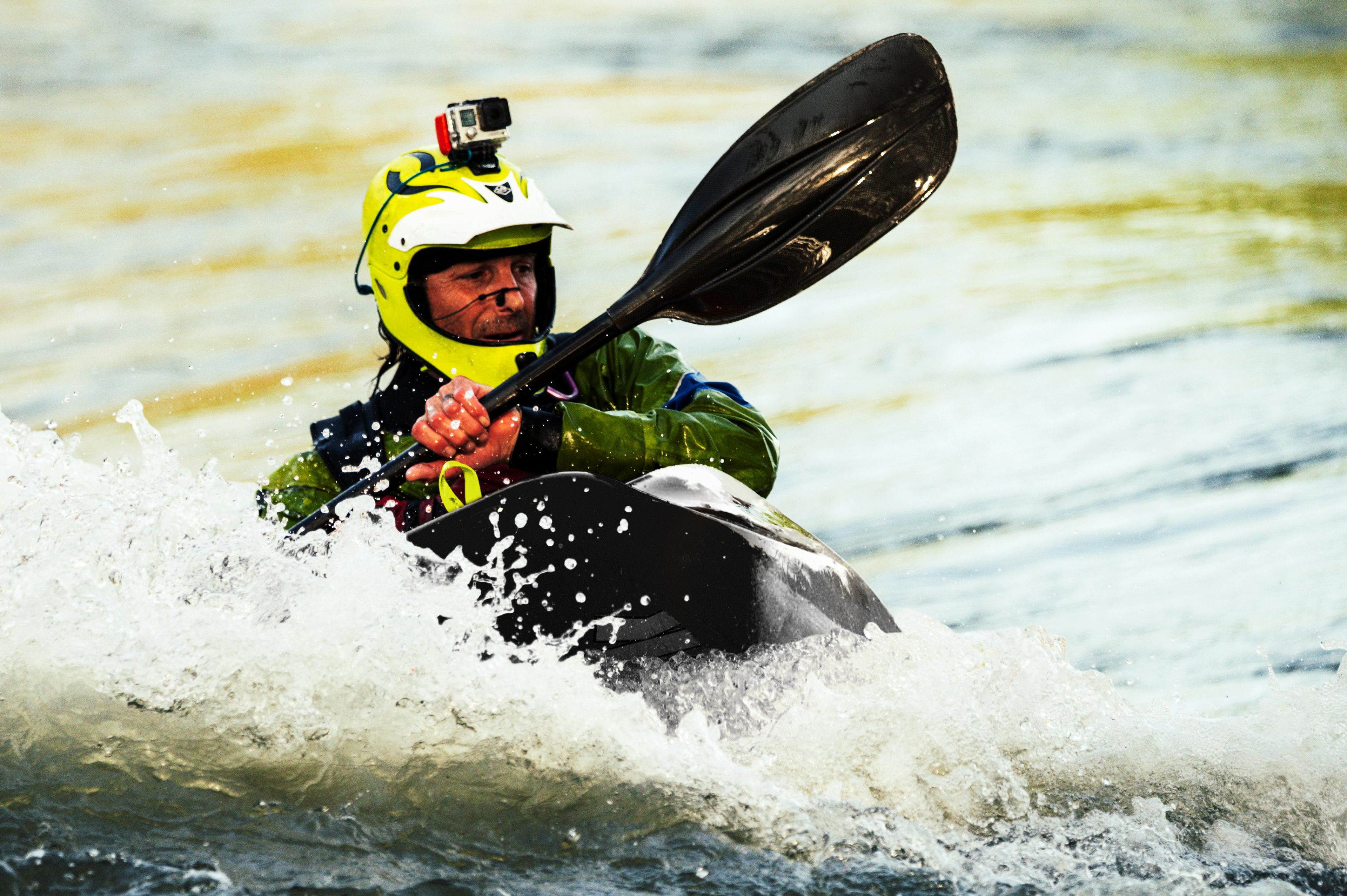 A man steers a kayak in a wave of water.