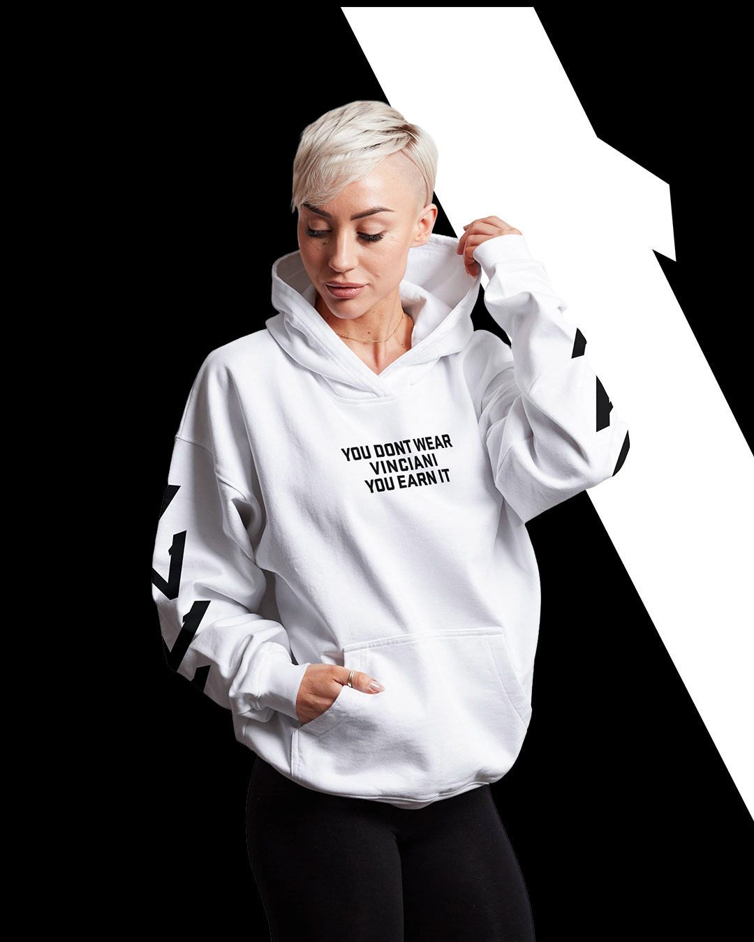 White hoodie featuring bold black slogan “YOU DON’T WEAR VINCIANI YOU EARN IT” on chest, worn by model in relaxed pose against a high-contrast black background with angular white graphic, showcasing Vinciani streetwear design.
