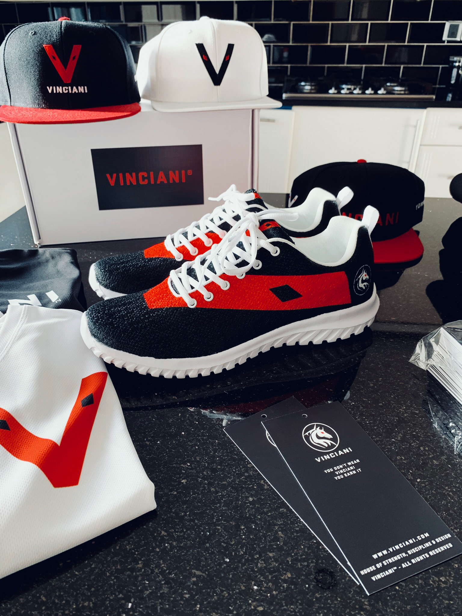 Vinciani Axiom Sneakers, Vinciani V Caps, and apparel dsiplayed together withy branded packaging and signature Code Red identity.