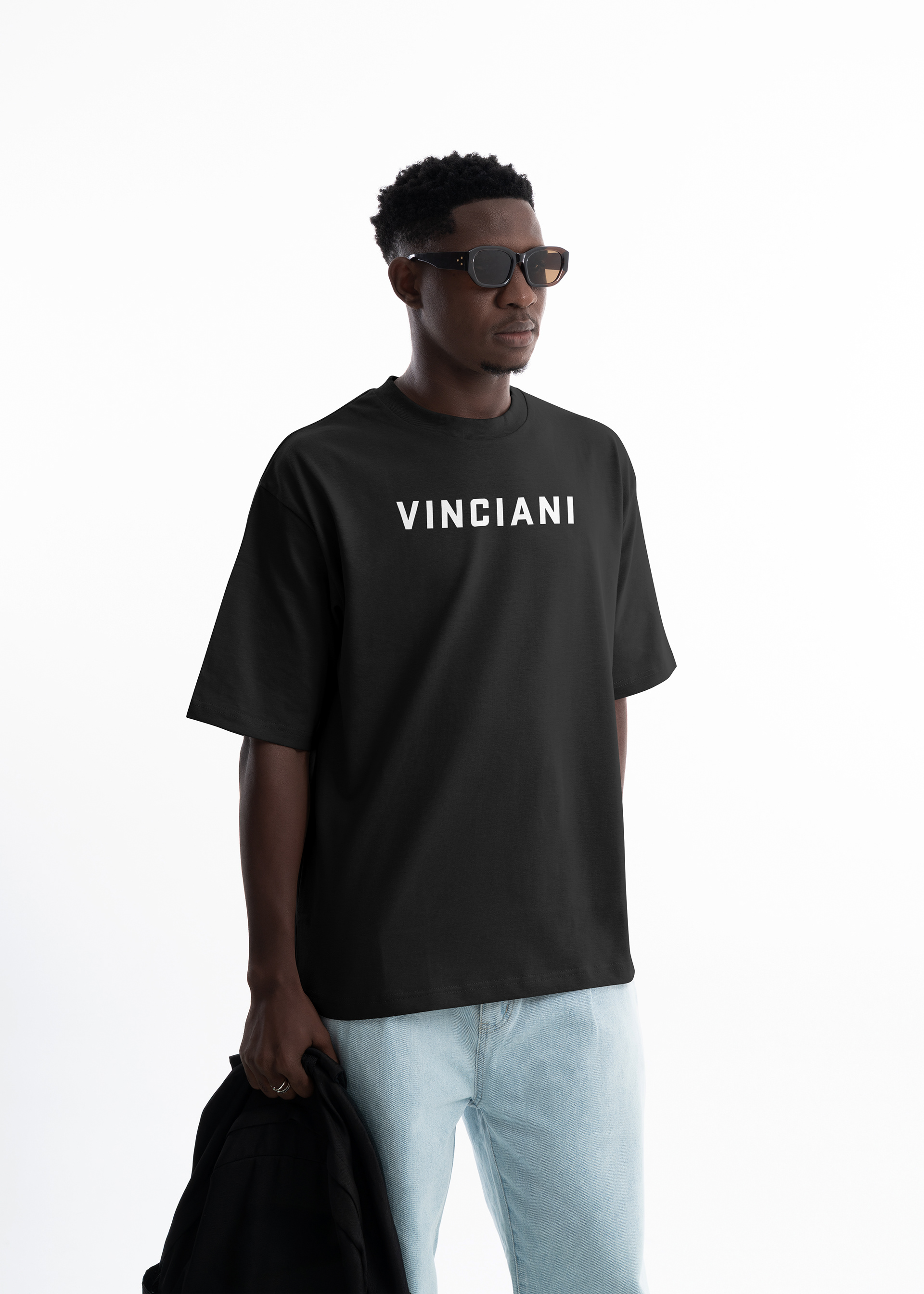 Male model wearing black Vinciani t-shirt with white logo, styled in a minimal studio setting representing Code White clarity and disciplined design.