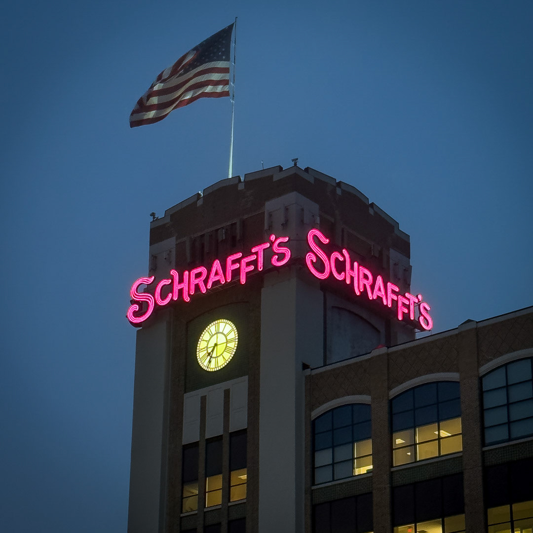 100. Schraffts Building Sign ••• The grand finale of the Boston Sign Project is the landmark Schrafft’s sign which is mounted atop the company’s former factory in Charlestown’s Sullivan Square. Schrafft’s was a candy, chocolate and cake company founded in 1861, and had stores and restaurants along the east coast up until the business was shut down in 1981. The old factory was converted into commercial office space, and in 2016 the famous neon sign was reconstructed exactly as it was with a high-efficiency, energy reducing lighting system. The sign remains an icon, and at night the pink neon glow can be seen for miles in all directions. (#100 of 100 in the Boston Signage Project)