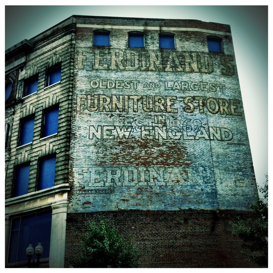 74. Ferdinands Furniture Ghost Sign ••• The iconic blue trim and flatiron design of Ferdinand's furniture store still dominates the area of Dudley Square, even though the building has been vacant since the 1990s. (#74 of 100 in the Boston Signage Project) ••• 2023 Update: The Ferdinand Building was restored and integrated into a new development called the Bruce C. Bolling Municipal Building. The sign was either covered up or destroyed.