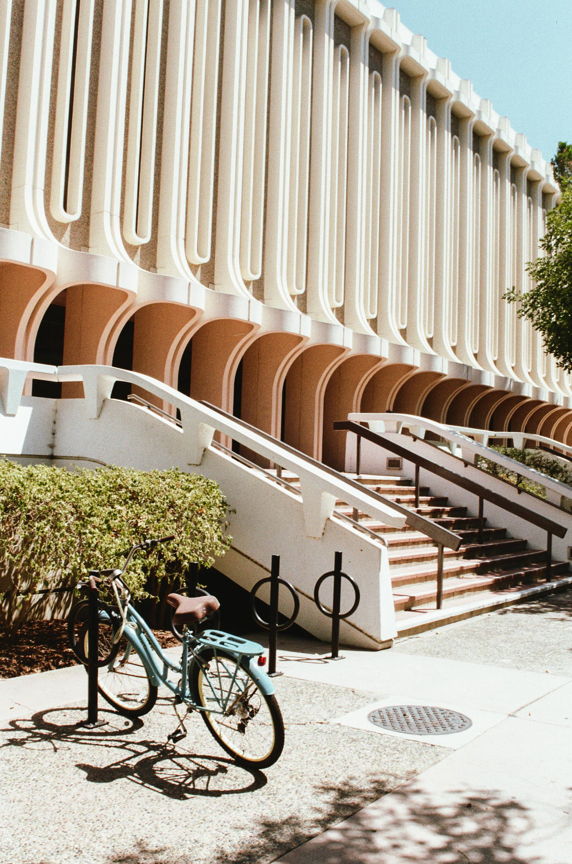 UC Irvine: A Nostalgic Touch – After spending the day exploring UC Irvine's campus, I stumbled across this scene in front of their library. While positioning my camera, I focused on the rule of thirds, leading lines, and framing the shadows and the building. I positioned the bike in the lower left third and tilted the camera so the sky, tree/bushes, and shadows could frame the scene. I am especially fond of the leading lines and the depth the building creates as it escapes behind the tree to the right.