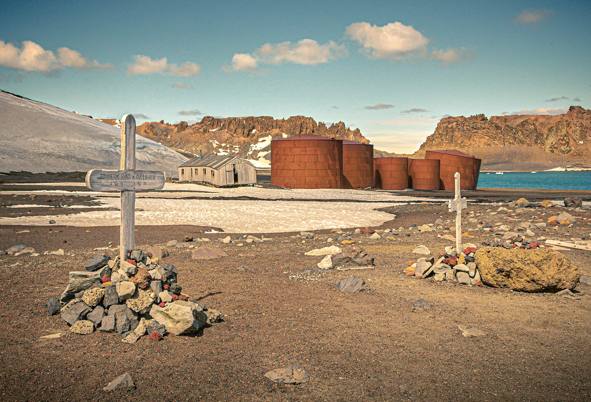 July 16, 2019Graveyard at Whalers Bay on Deception Island which is part of the South Shetland Islands in Antarctica.The grave on the left is for Hans Albert Gulliksen born 7/4 1871, died 4/1 1928. At the time of his death, he was working in the whaling industry as a carpenter, as indicated by the title "Tømmerm." used on his grave marker.These two graves are the only ones that survived a volcanic eruption on Deception Island in 1969. The cemetery is an official Historic Site or Monument, Number 71, in accordance with the Antarctic Treaty that was entered into force in 1961.