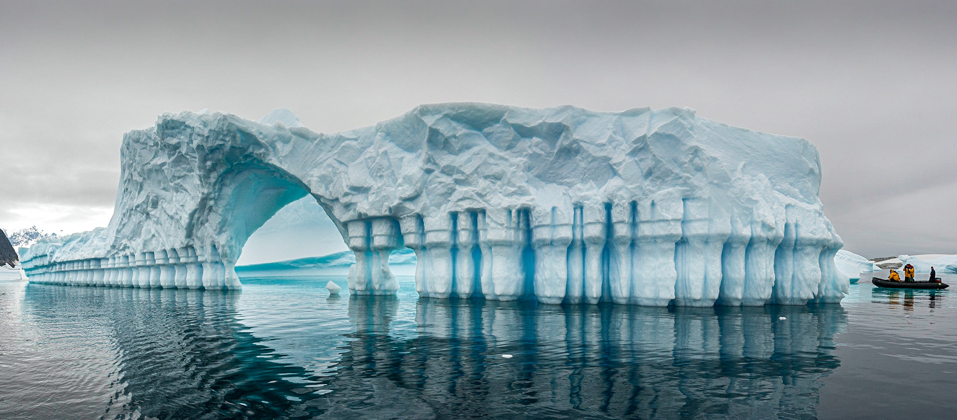 August 16, 2020A remarkable iceberg found in the “Iceberg Graveyard” just off Pléneau Island near the Lemaire Channel, Antarctica.The columns are a result of natural seawater erosion. The interesting aspect of the Iceberg Graveyard is that these bergs are grounded–which means they can't float away nor capsize which is a major danger and one reason why Zodiac cruises don't approach large icebergs. You never know when a berg will roll over.If you are in a Zodiac near a berg when it rolls over, you run the very real risk of having your Zodiac flooded or capsized. With the water temp near freezing, you might not survive in the water for the period of time it might take to rescue you.Which is why the expedition crew used to joke about our life preservers–which auto inflate when they hit seawater-aren't so much "life preservers" and more like "body recovery devises". But since these bergs are grounded, we were able to get really close. In fact my bunkmate Seth Resnick talked the Zodiac driver to go into the arch so he could get a shot.That particular cruise was launched with the instructors on the cruise while we shot a video commemorating the launch and shipping of Lightroom 1.0 on February 19th, 2007. In our boat was Michael Reichmann, John Paul Caponigro, Seth Resnick, Ian Lyons, Bill Atkinson, Stephen Johnson and our videographer Chris Sanderson. Our Zodiac driver was Robert "has anybody seen a big white boat" Gilmore.