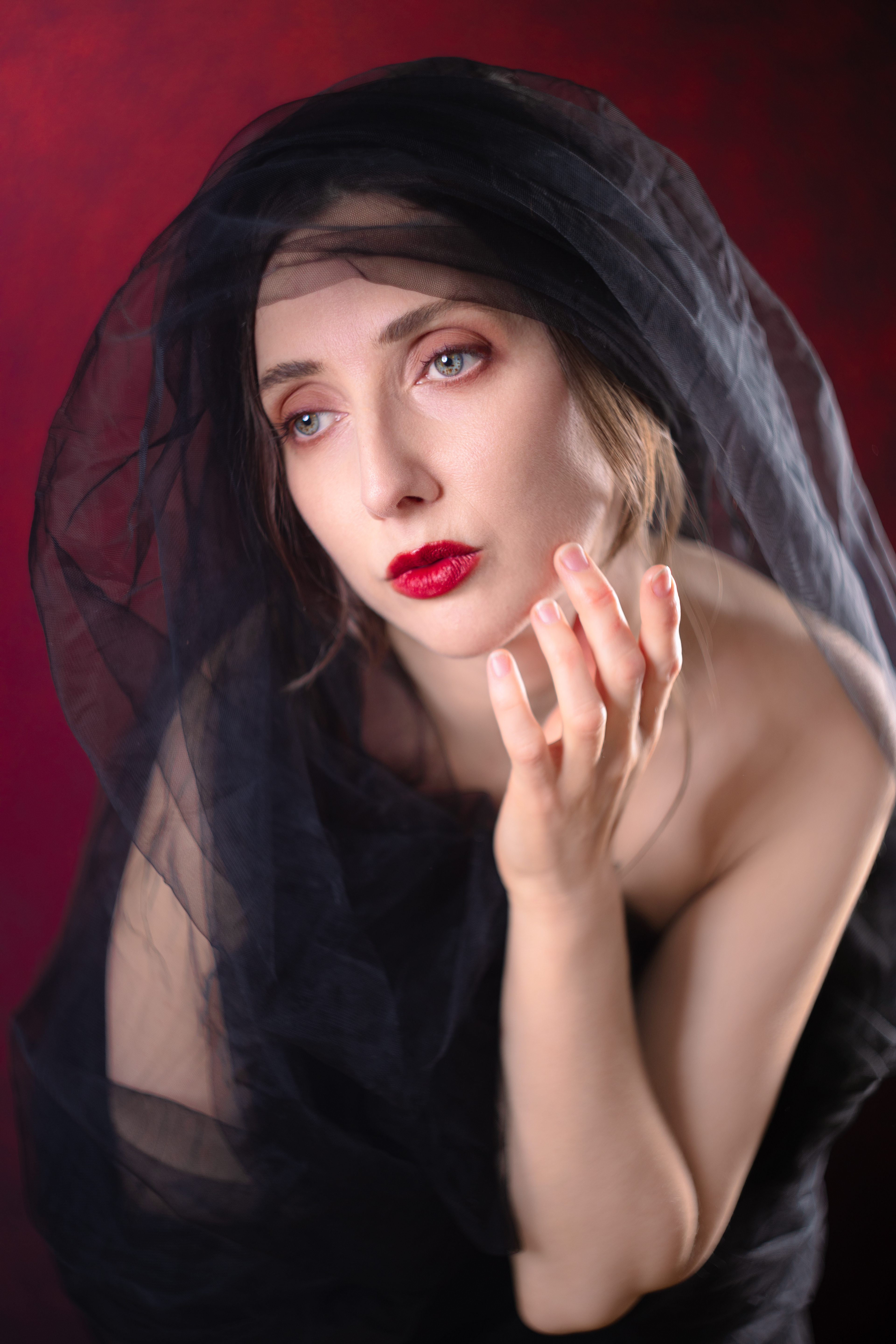 Head and shoulders closeup of a beautiful woman wearing a black veil against a red background. The woman's brown-flecked green and blue eyes are noticeable. This picture was taken using a film lens modified to fit a digital camera.
