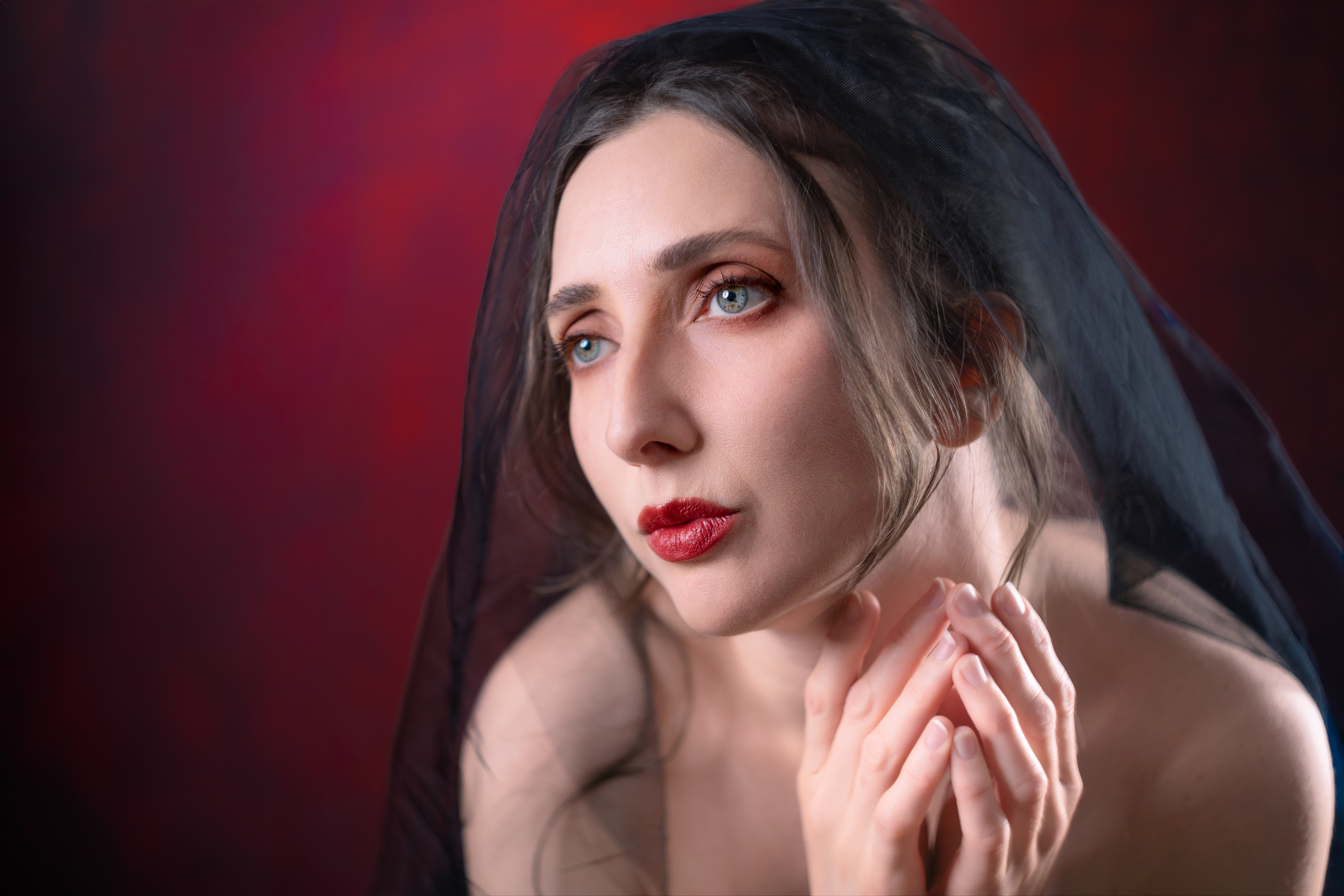 Head and shoulders closeup of a beautiful woman wearing a black veil against a red background. The woman's brown-flecked green and blue eyes are noticeable. This picture was taken using a film lens modified to fit a digital camera.