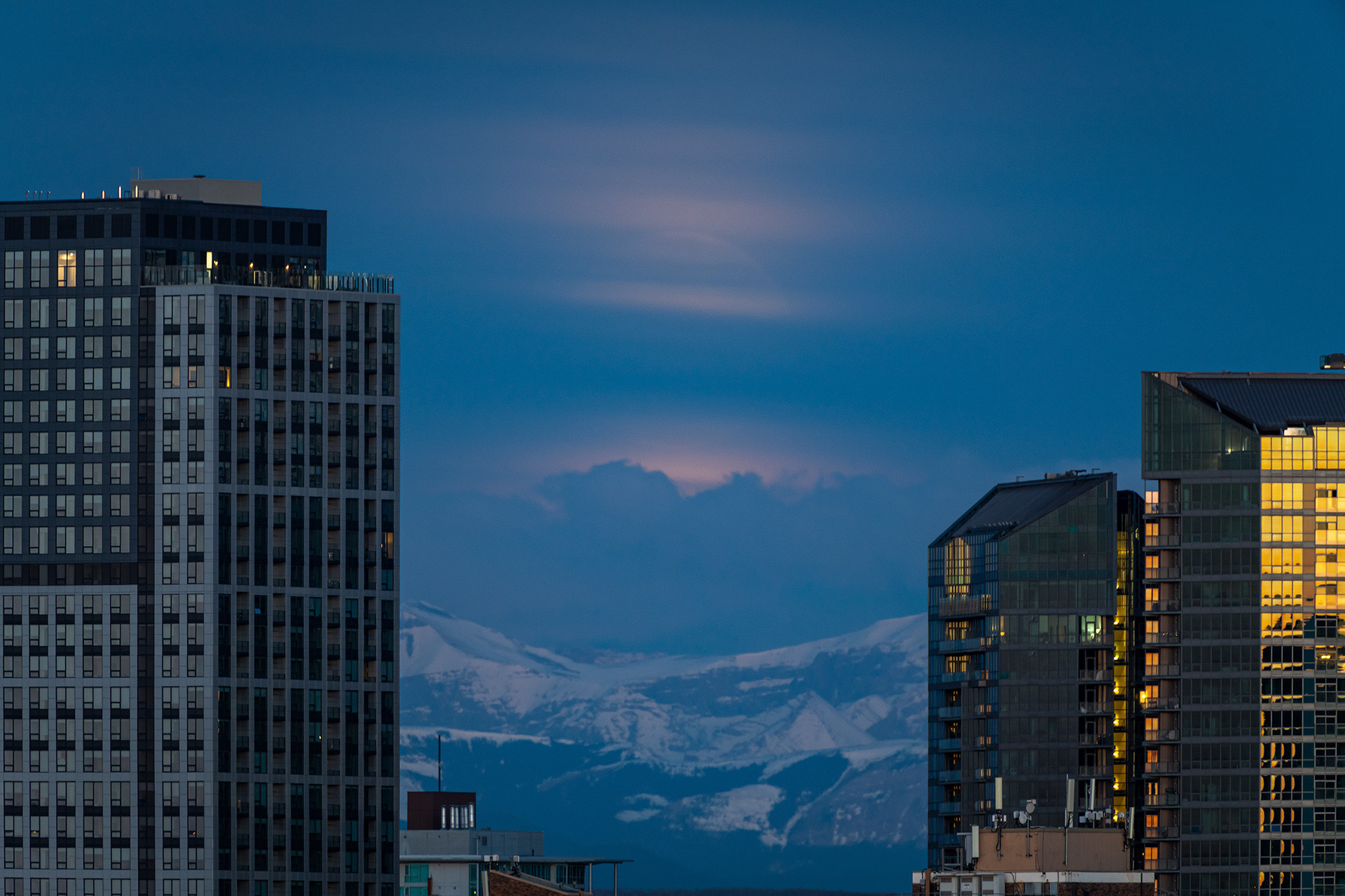 Moonset (Full phase @ 99.3%, elevation 1.9 degrees) (Civil Twilight, Sun elevation -4.9 degrees) over the Rocky Mountains, and between downtown buildings, Tom Campbell's Hill Natural Park, Calgary, AB