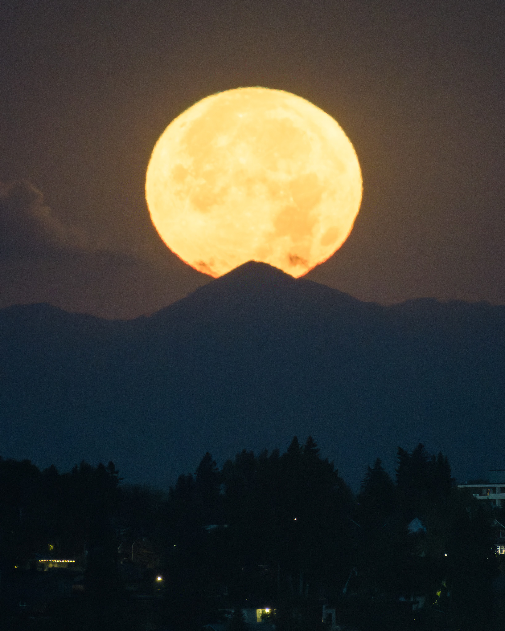 Photo of the setting Sturgeon Moon over the distant Rocky Mountains, from the Crescent Heights Lookout Point, Calgary, AB - August 19th