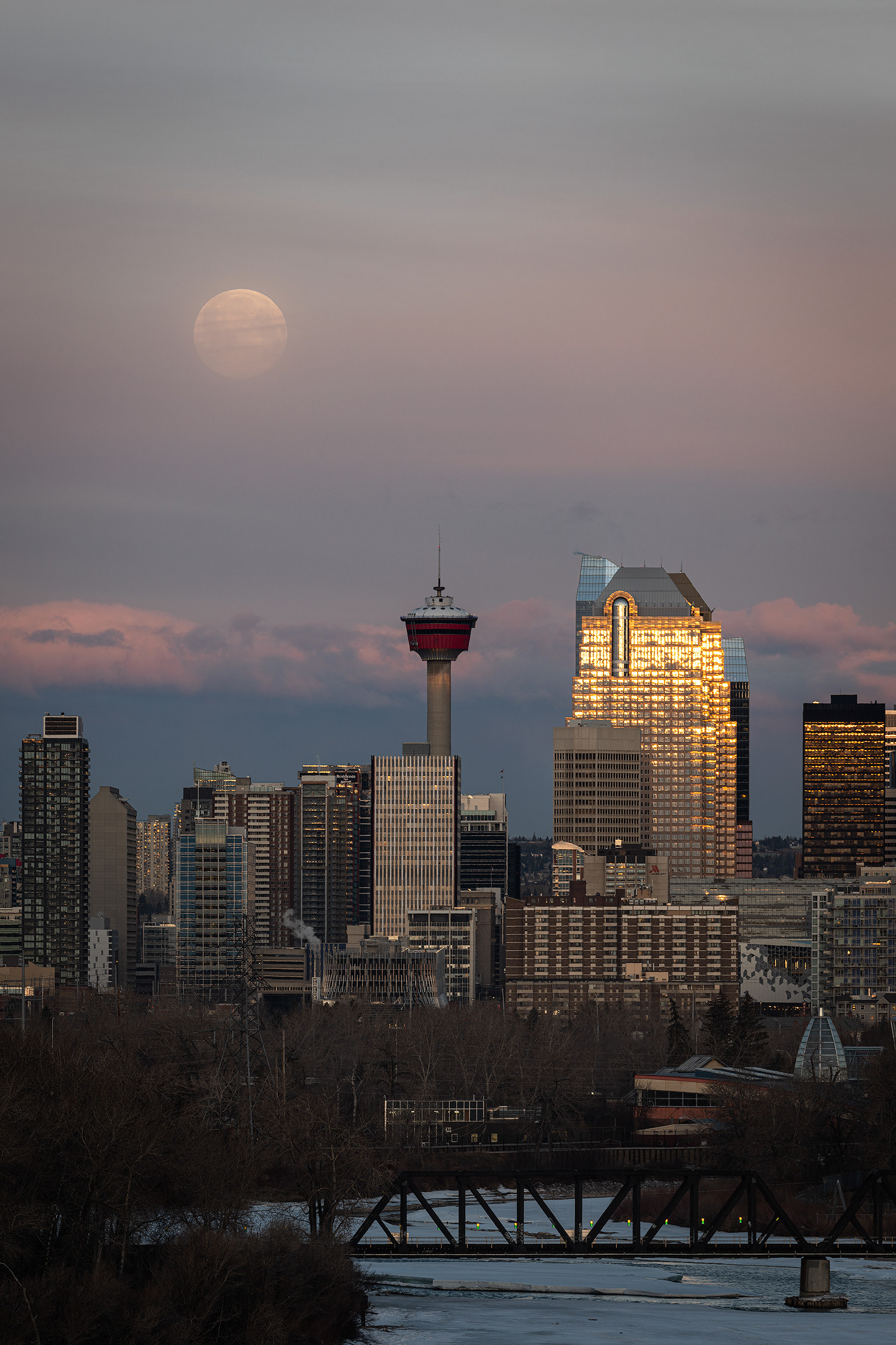 Cityscape of a portion of the downtown skyline, Bow River, and setting Full Moon at Sunrise (sun altitude 0.9 degrees), from near Max Bell Centre, Calgary, AB