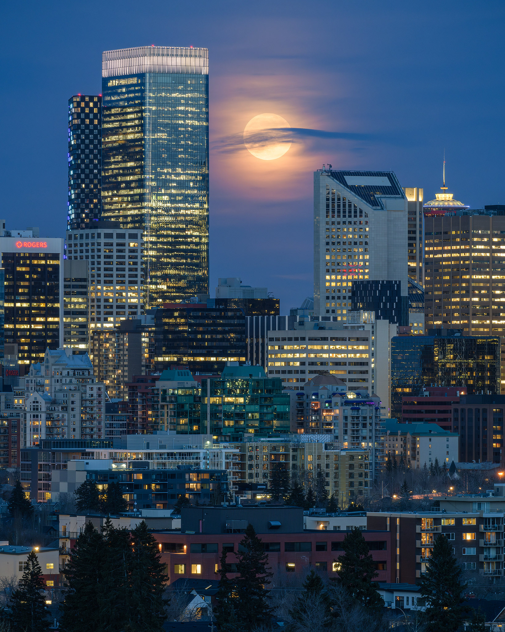 A photo of the Moon rising beyond a portion of the Downtown Calgary skyline during Civil Twilight, from West Hillhurst, Calgary, AB - April 23rd