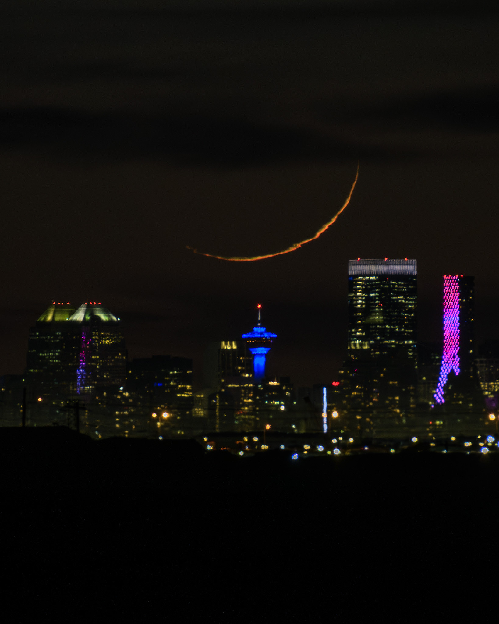 A photo of the Moon setting beyond a portion of the Downtown Calgary skyline during Nautical Twilight, from near Indus, AB - May 8th