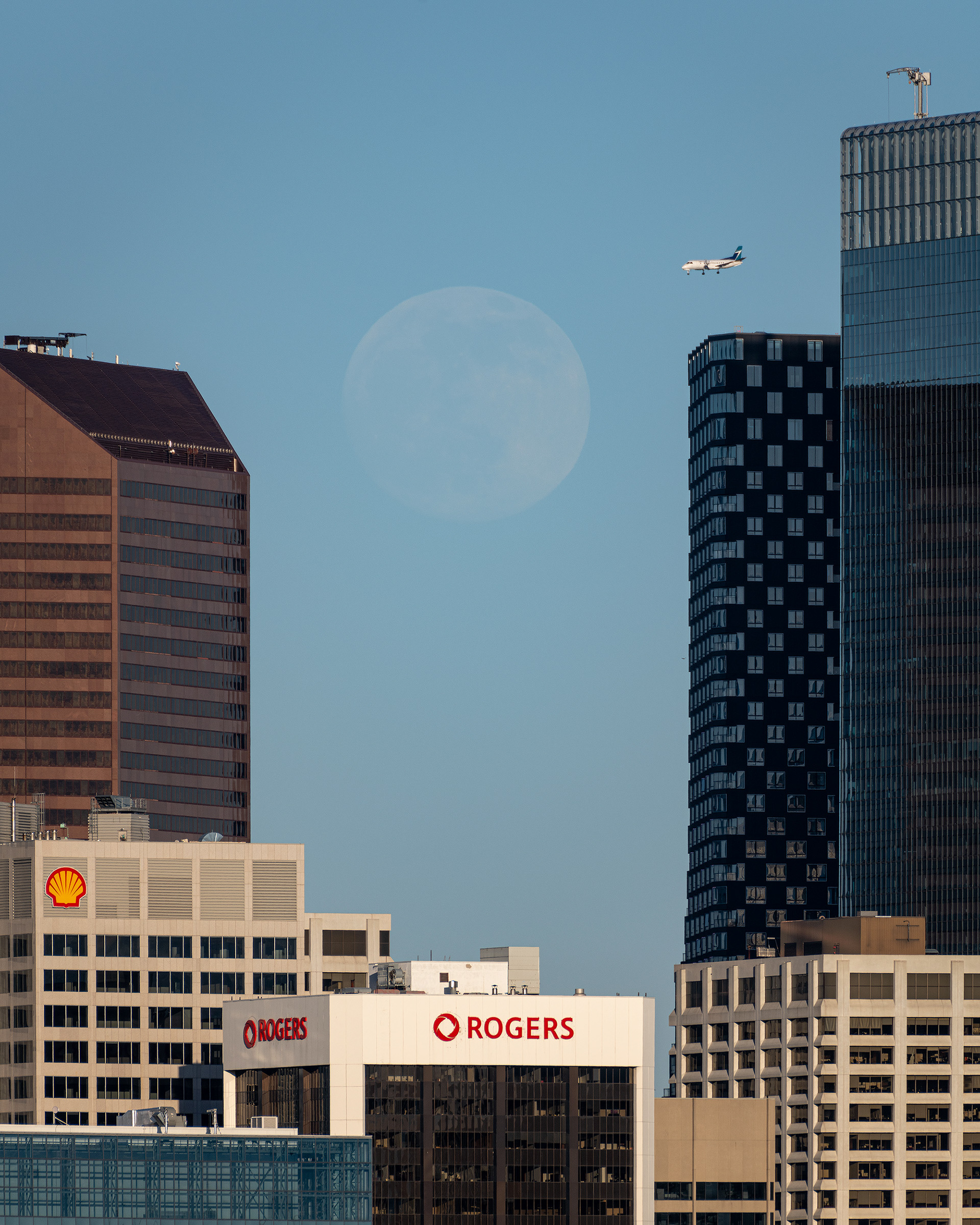 Moonrise (Waxing Gibbous phase @ 98.3%, elevation 2.75 degrees) between some familiar downtown buildings, from Grasshopper Hill, West Hillhurst, Calgary, AB