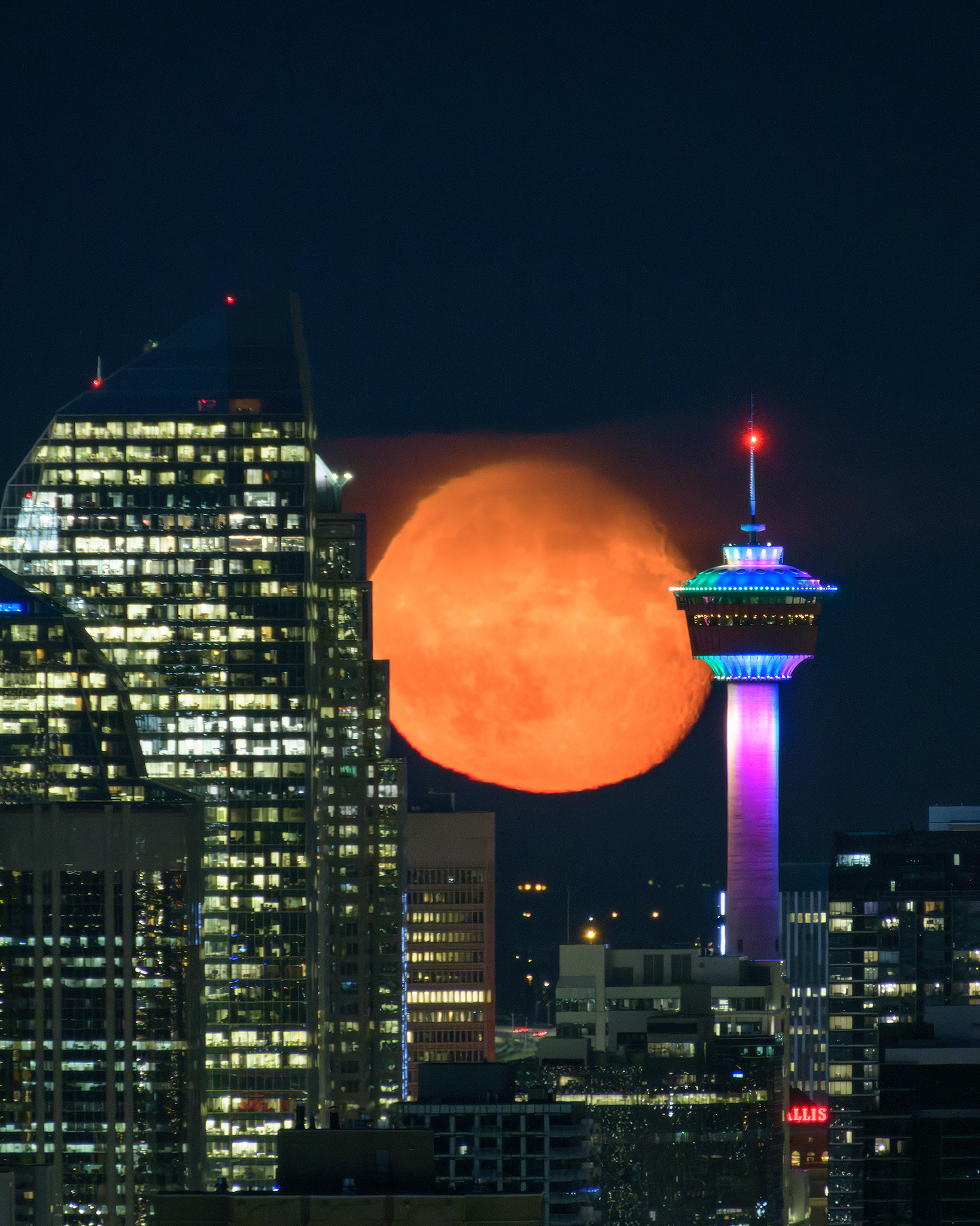 Photo of the rising Moon (Waning Gibbous, 91.8%) squeezing up between Eighth Avenue Place and the Calgary Tower, from nearly 8 kms away, Strathcona, Calgary, AB - August 21st