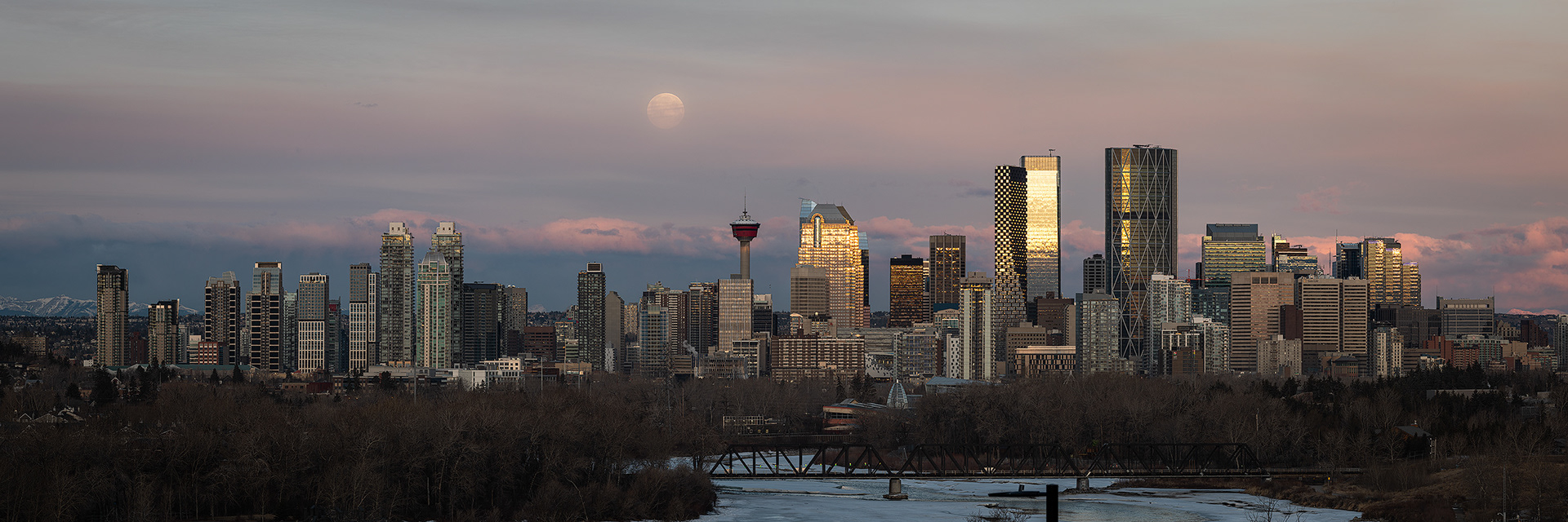 3x1 Panoramic Cityscape (22 shot, 2 row) of the downtown skyline, Bow River, and setting Full Moon at Sunrise (sun altitude 0.9 degrees), from near Max Bell Centre, Calgary, AB